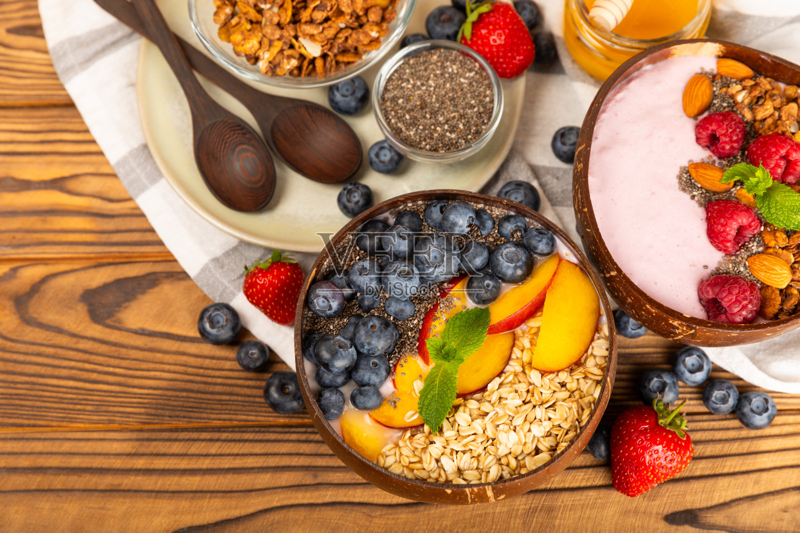 在厨房的桌子上，有一碗酸奶和新鲜的杏仁、蓝莓、覆盆子、桃子和草莓。巴西莓和螺旋藻碗。健康早餐概念。副本的空间。放文字的地方。照片摄影图片