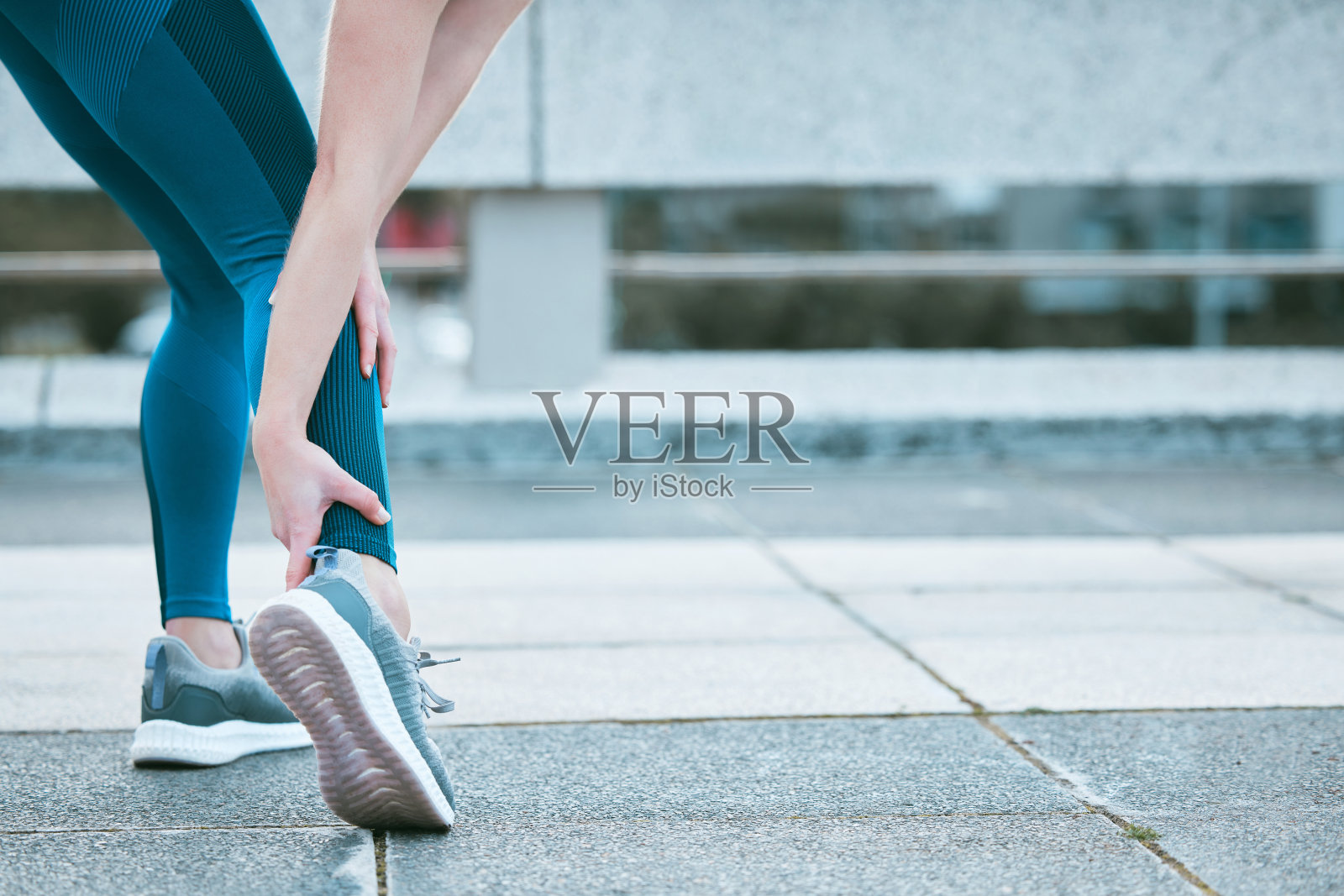 一个白人妇女抱着她疼痛的脚踝在户外锻炼的特写。女运动员在训练中因脚部骨折和肌肉发炎而疼痛。与引起不适和紧张的僵硬的身体抽筋斗争照片摄影图片