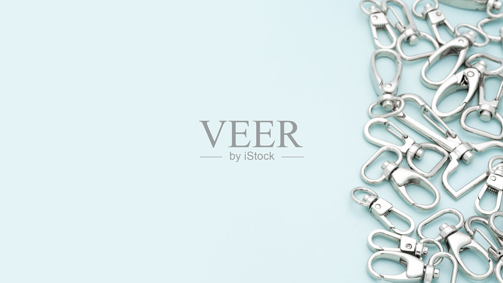 淡蓝色背景上放着一堆用来制作包和背包的金属龙虾爪扣。包、背包用镀铬金属配件及用品。手袋制作，拷贝空间照片摄影图片