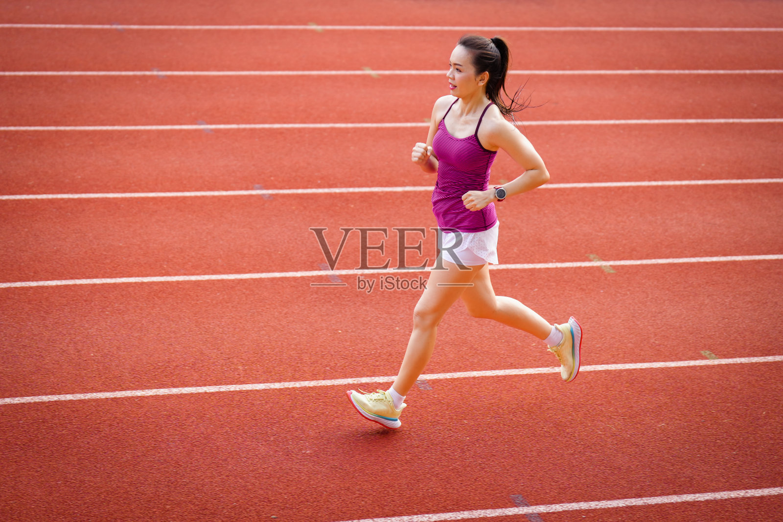 亚洲中年妇女在阳光明媚的早晨在体育场跑道上跑步照片摄影图片