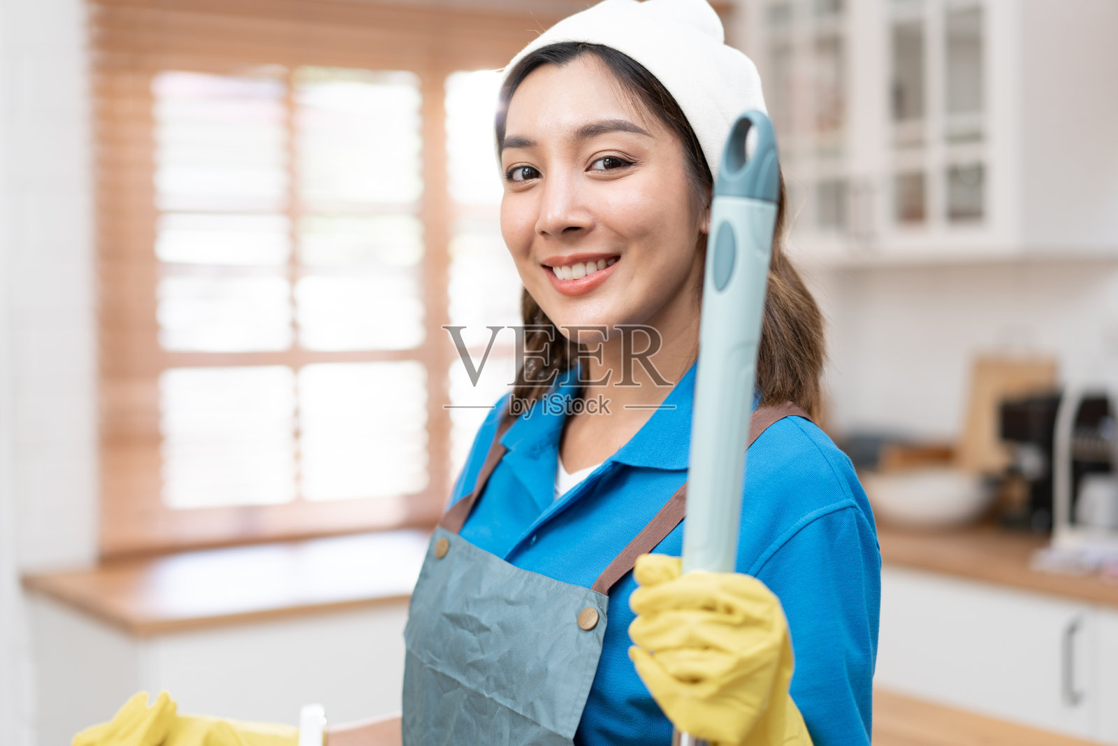 肖像亚洲年轻女子在厨房里拿着拖把，穿着女仆制服照片摄影图片