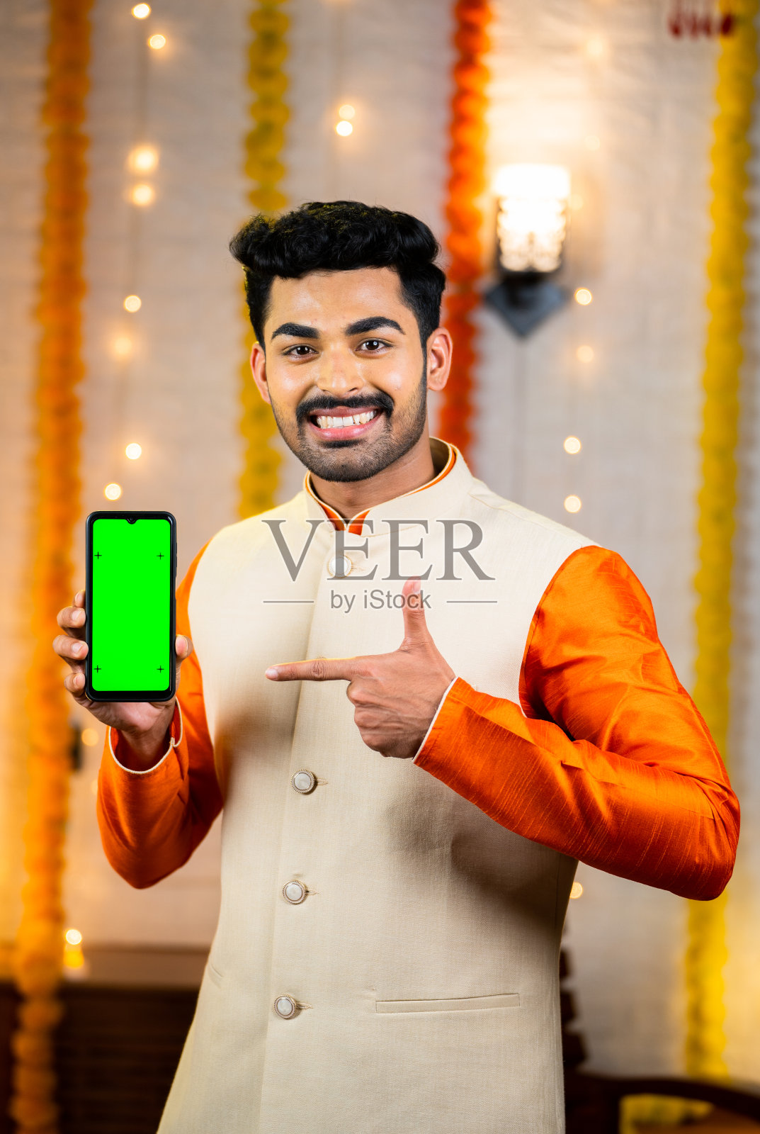 垂直拍摄快乐的印度人穿着传统民族服装，用手指指着绿屏手机，看着相机- app或应用程序，促销，节日销售和优惠的概念照片摄影图片