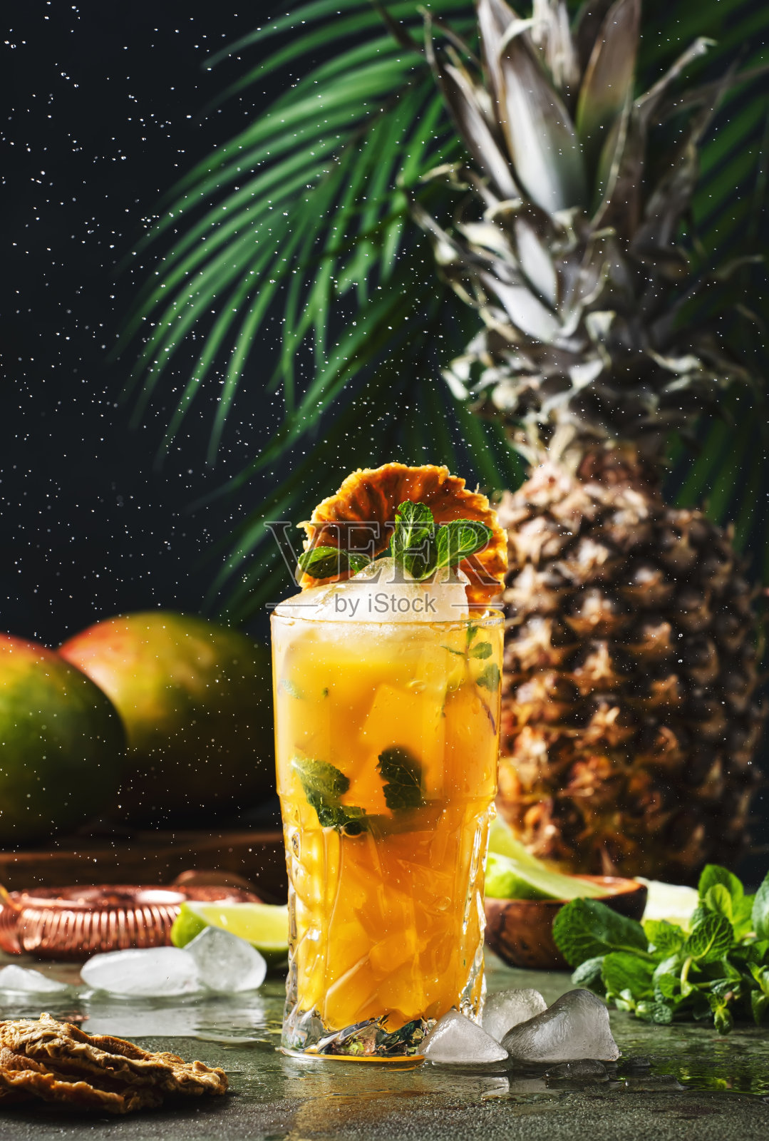夏季鸡尾酒配伏特加，菠萝汁，芒果，冰。长饮或冷饮。冰冻的水花和飞落。热带背景，棕榈叶照片摄影图片