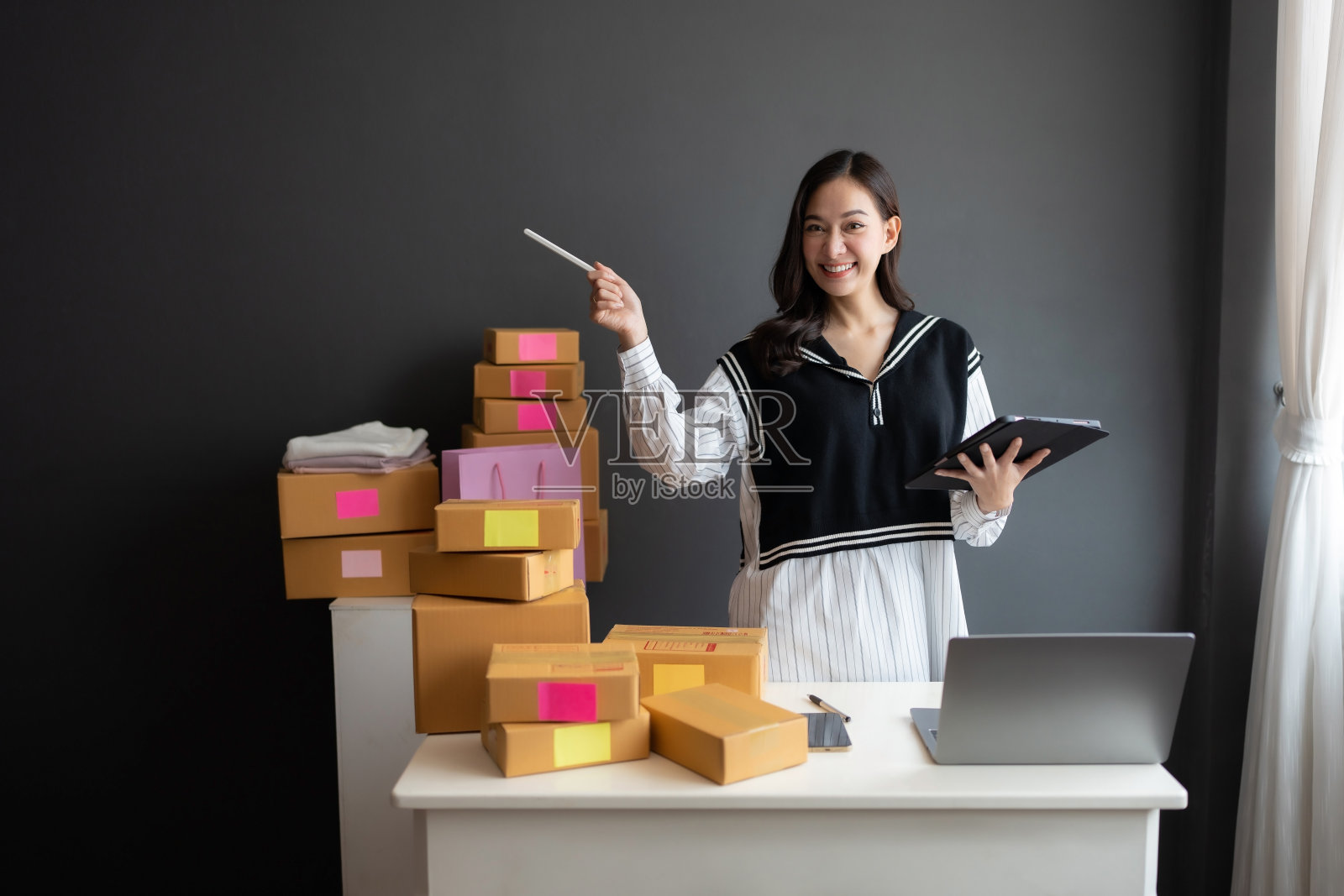 我很高兴她的生意能够卖产品。顾客的销售情况很好。她手里拿着一块写字板和一支笔。有产品盒和购物袋。照片摄影图片