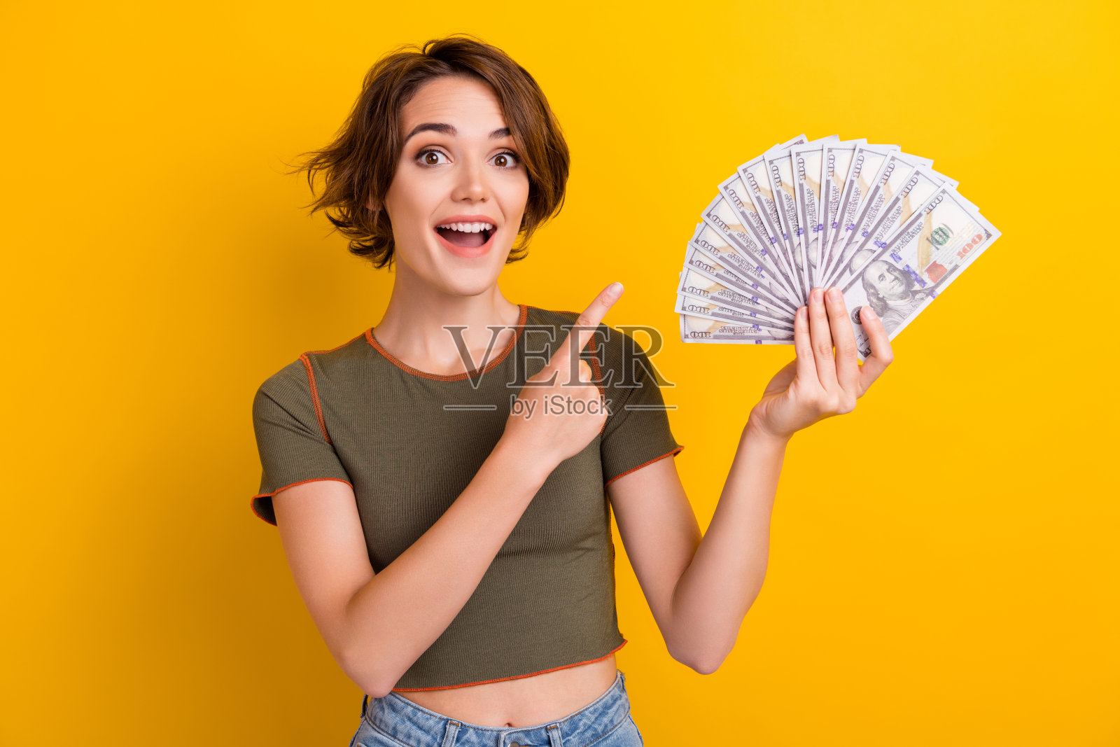 印象深刻的惊讶女人的肖像，短发，卡其色上衣，黄色背景上孤立的一束钱照片摄影图片