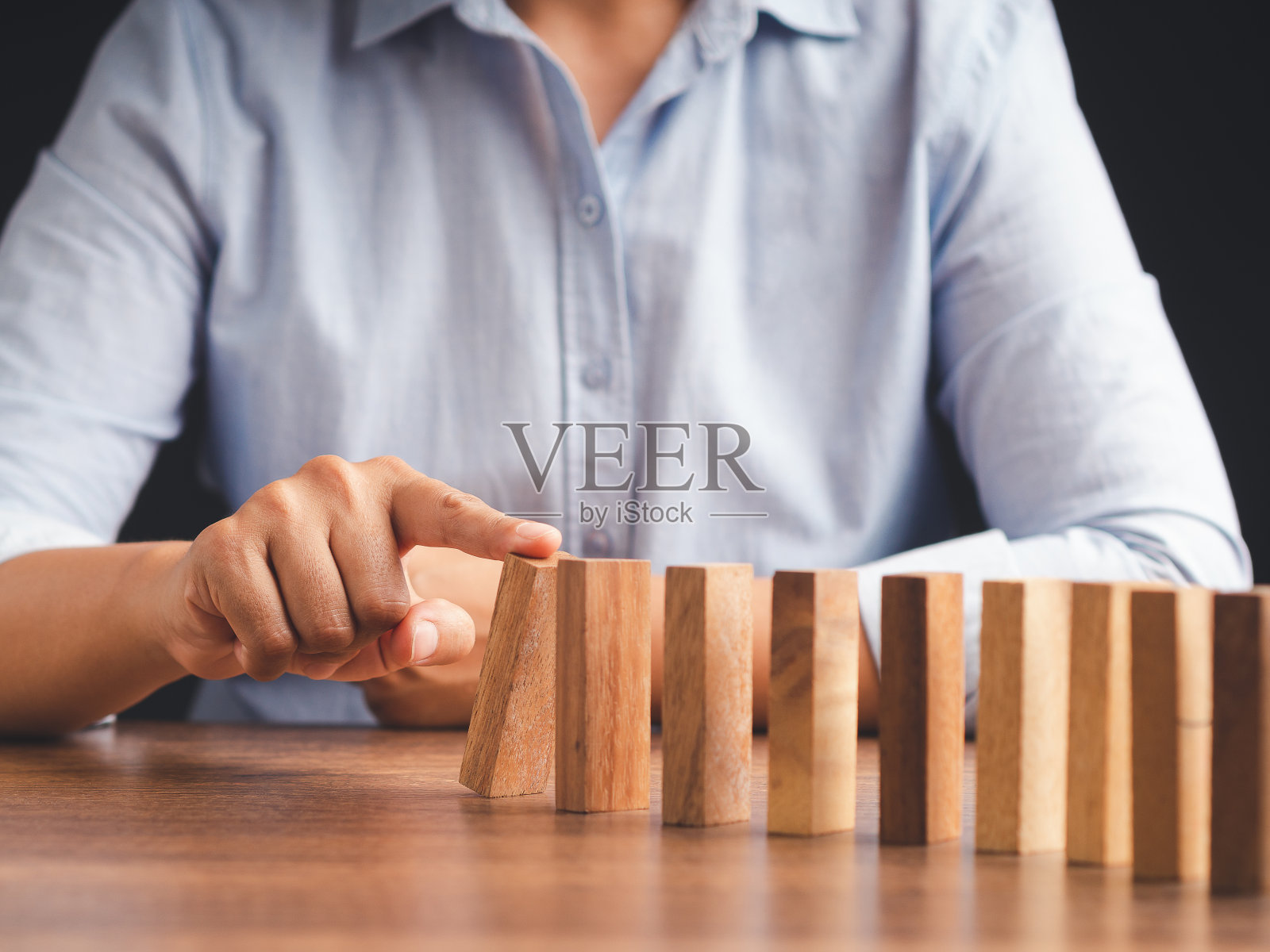 一个商人坐在办公室里推着一排多米诺骨牌上的木块的手。照片摄影图片