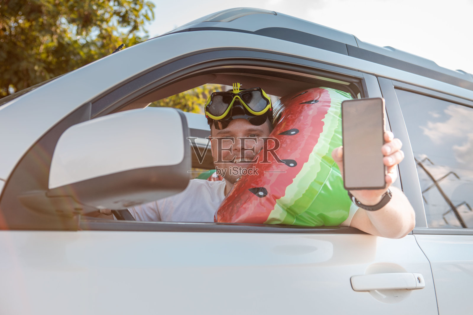 开车载满度假物品、拿着白色屏幕手机的快乐男人照片摄影图片