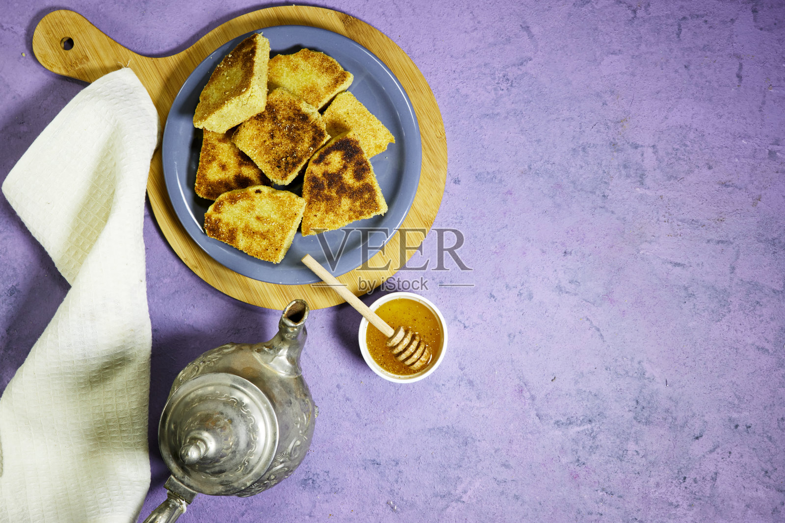 在砧板上方的阿拉伯式彩色盘子上放着阿尔及利亚粗面粉煎饼。传统阿尔及利亚早餐面包配蜂蜜碗照片摄影图片