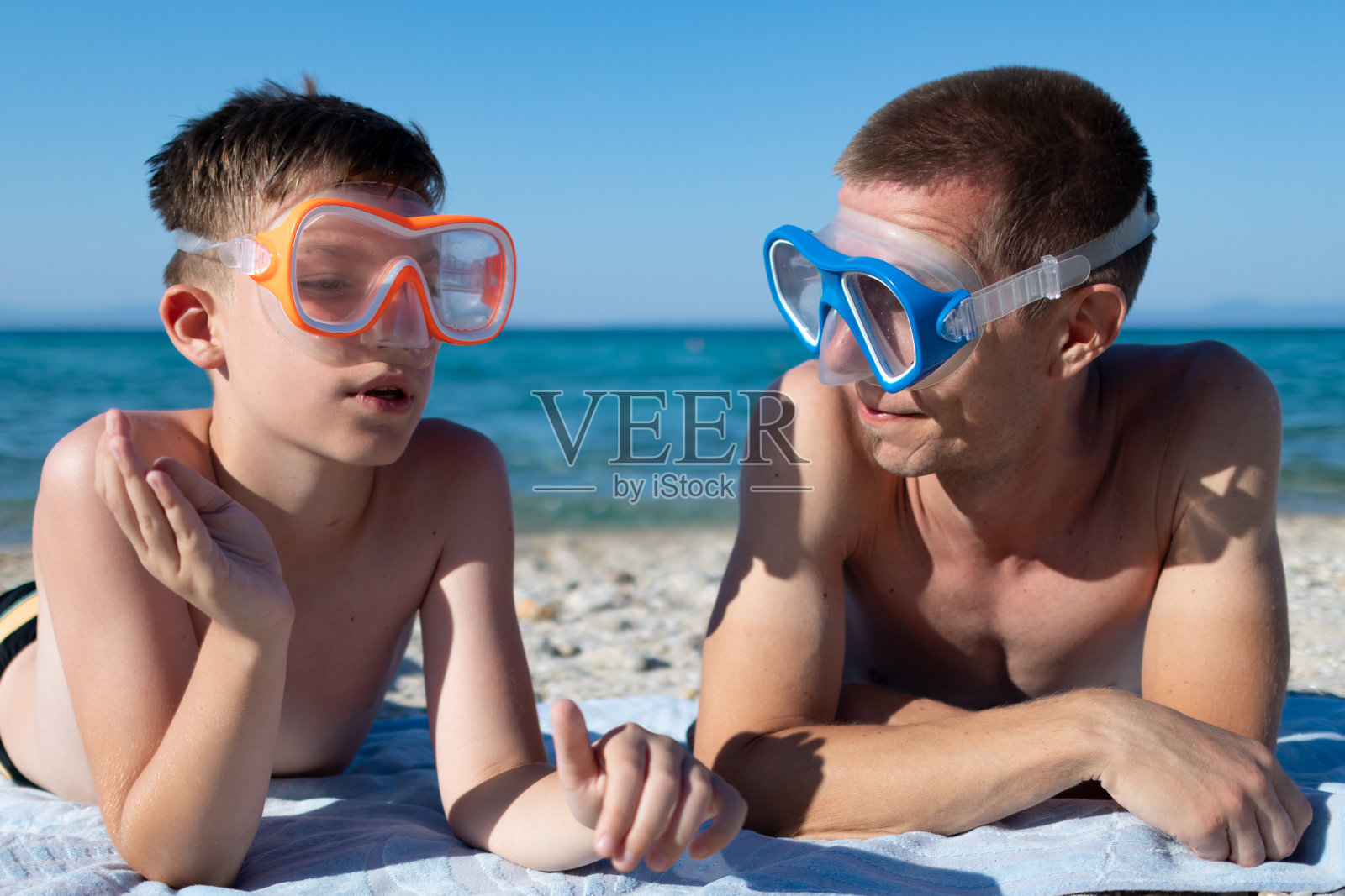 快乐的父子带着潜水面罩准备在海洋里浮潜。照片摄影图片