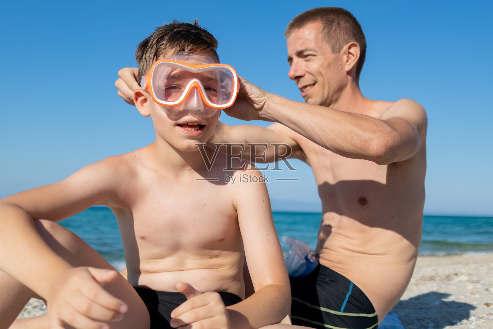 快乐的父子带着潜水面罩准备在海洋里浮潜。照片摄影图片