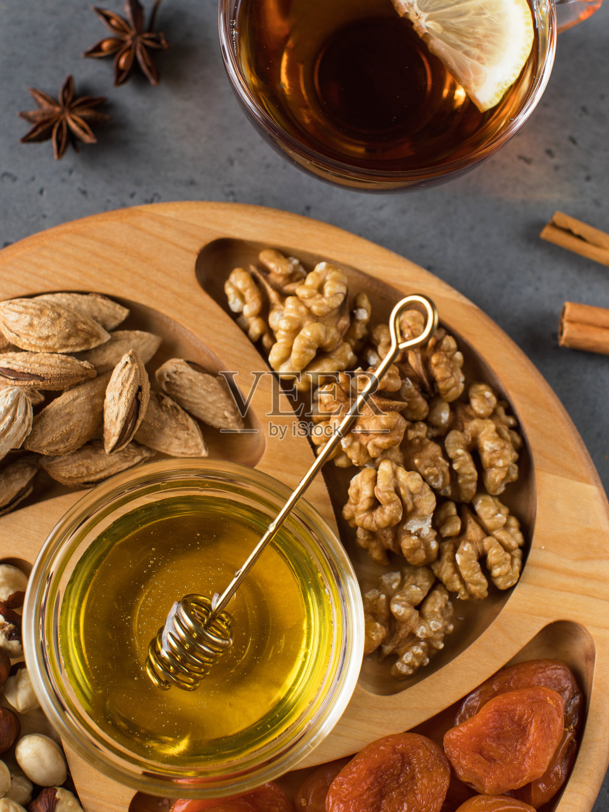 什锦坚果和杏干放在木盘上，配上蜂蜜和一杯茶。照片摄影图片