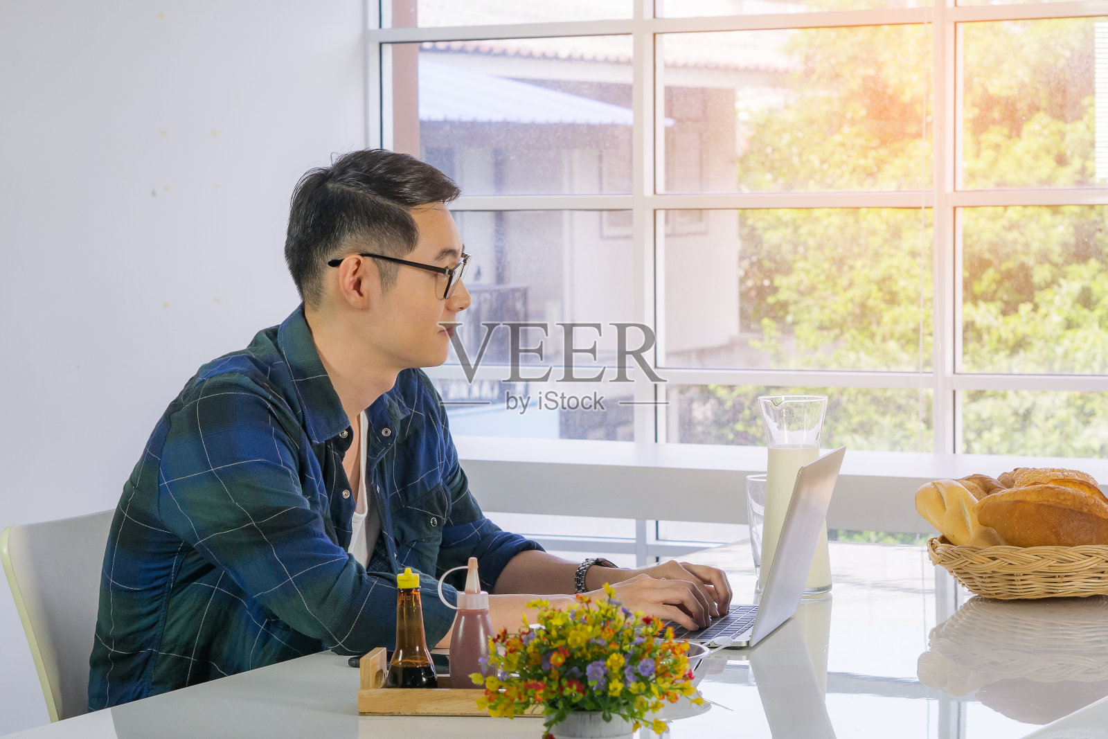 年轻人正在厨房用笔记本电脑工作。照片摄影图片