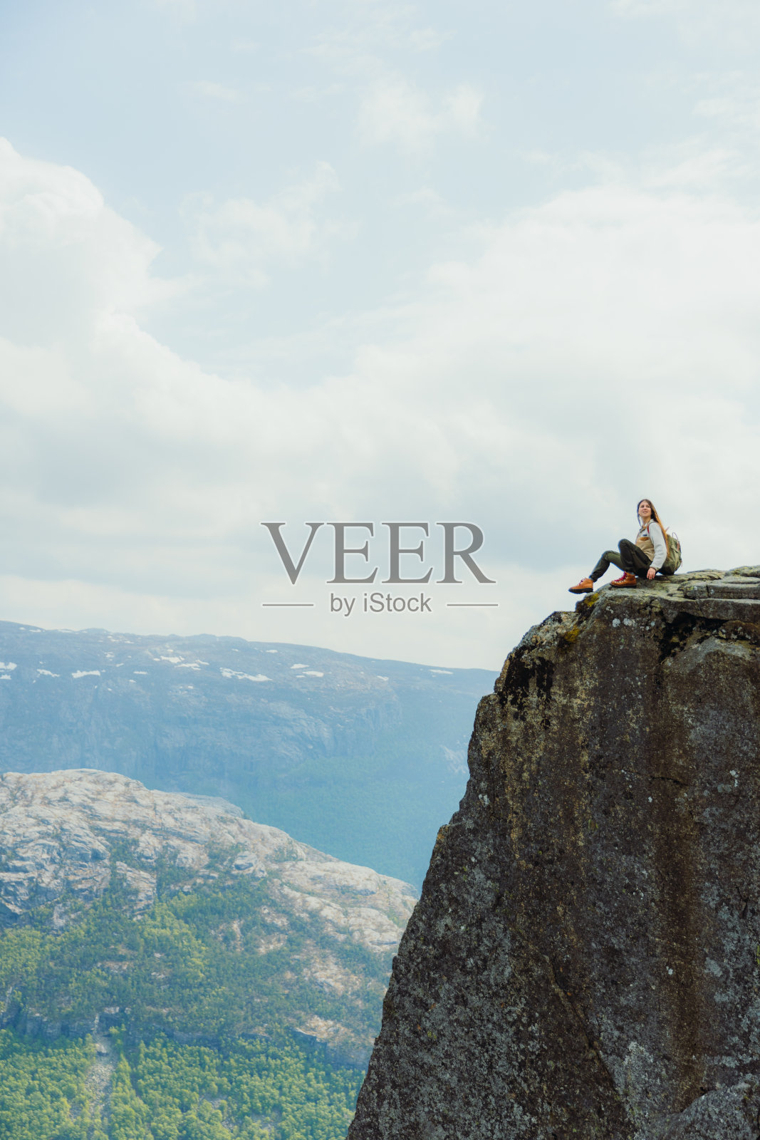 背着背包的女人坐在布道石山上，凝视着挪威的美景照片摄影图片