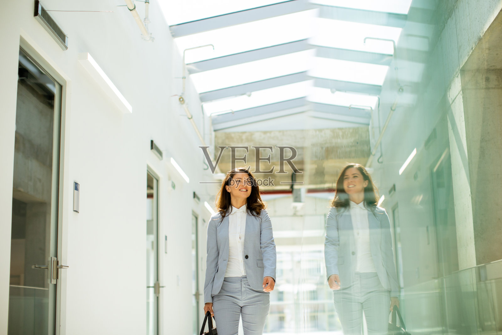 年轻漂亮的女商人提着公文包走在办公室走廊上照片摄影图片