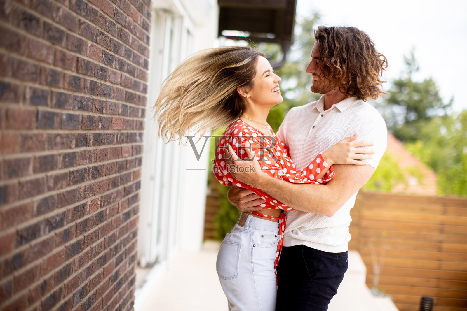 微笑的年轻情侣站在房子的砖墙前照片摄影图片