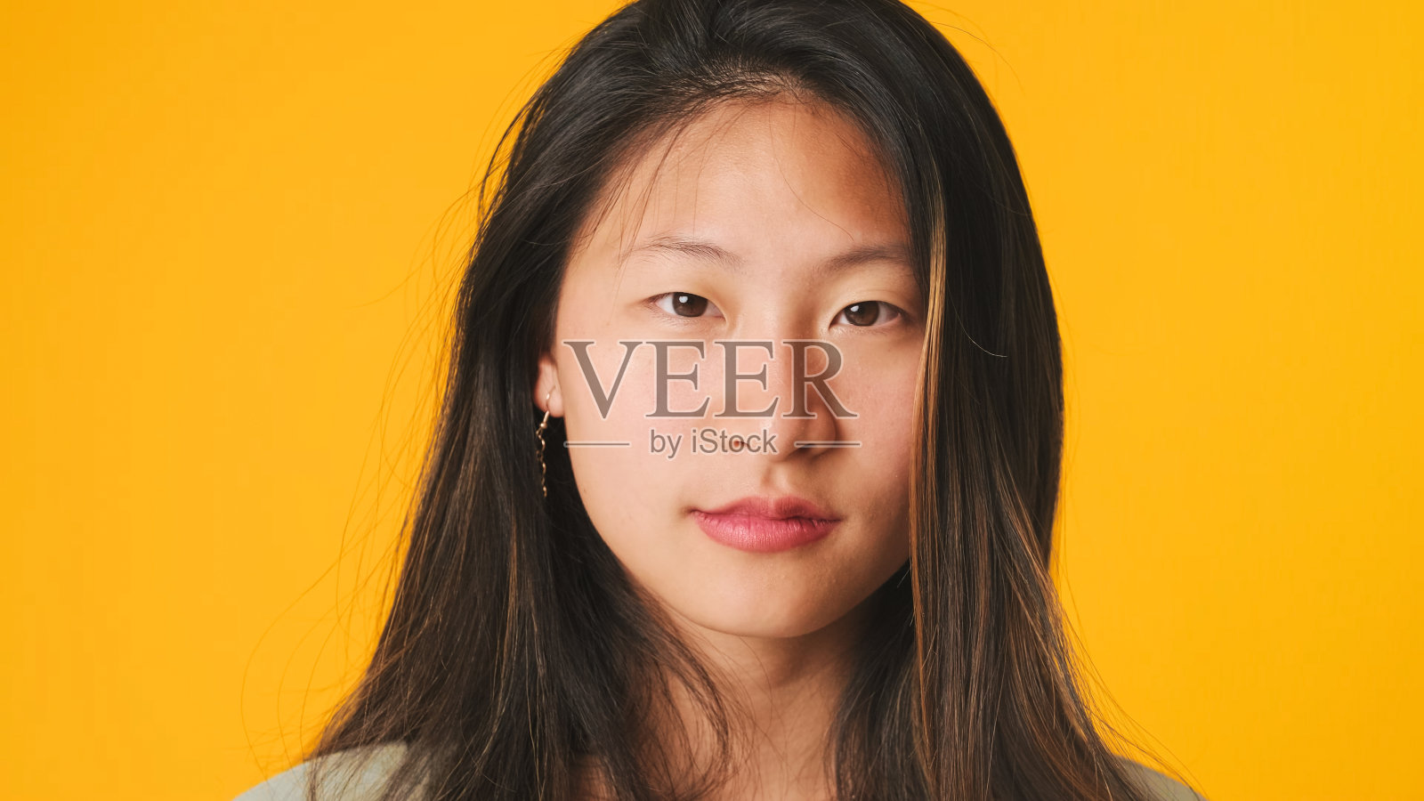 特写，穿灰色上衣的女孩被孤立在黄色背景上，看着镜头照片摄影图片