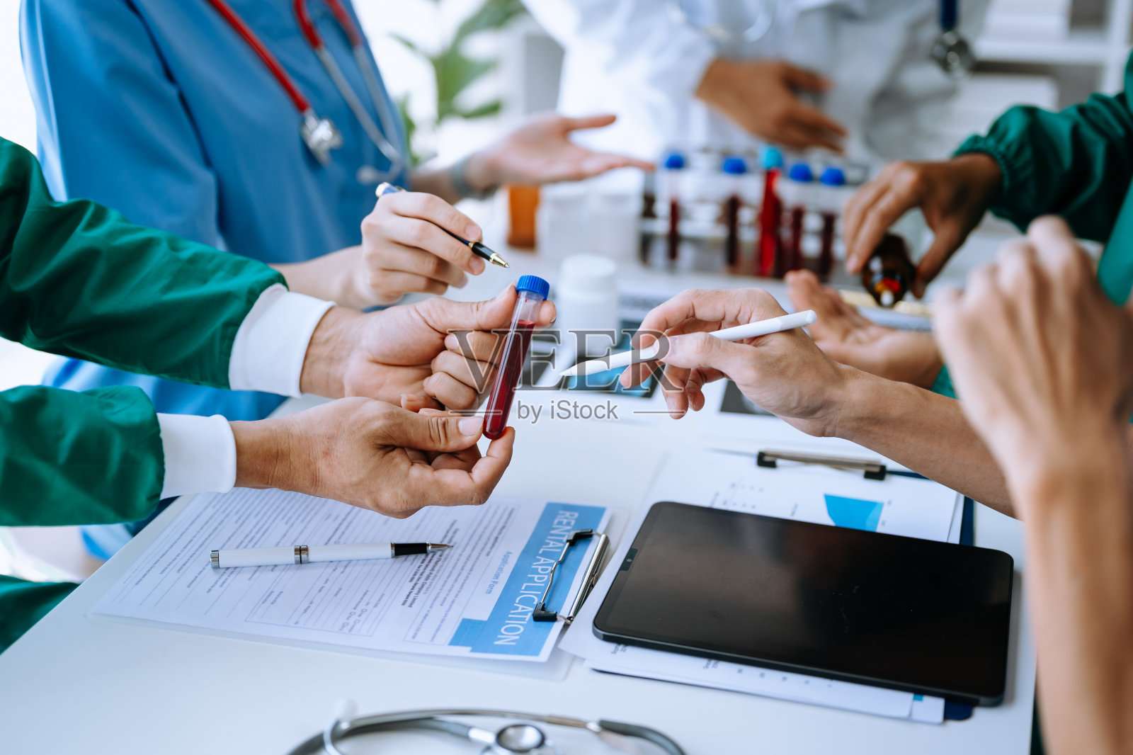 医疗团队正在开会，穿着白大褂和外科手术服的医生们坐在桌子旁，讨论用电脑在线工作的病人照片摄影图片