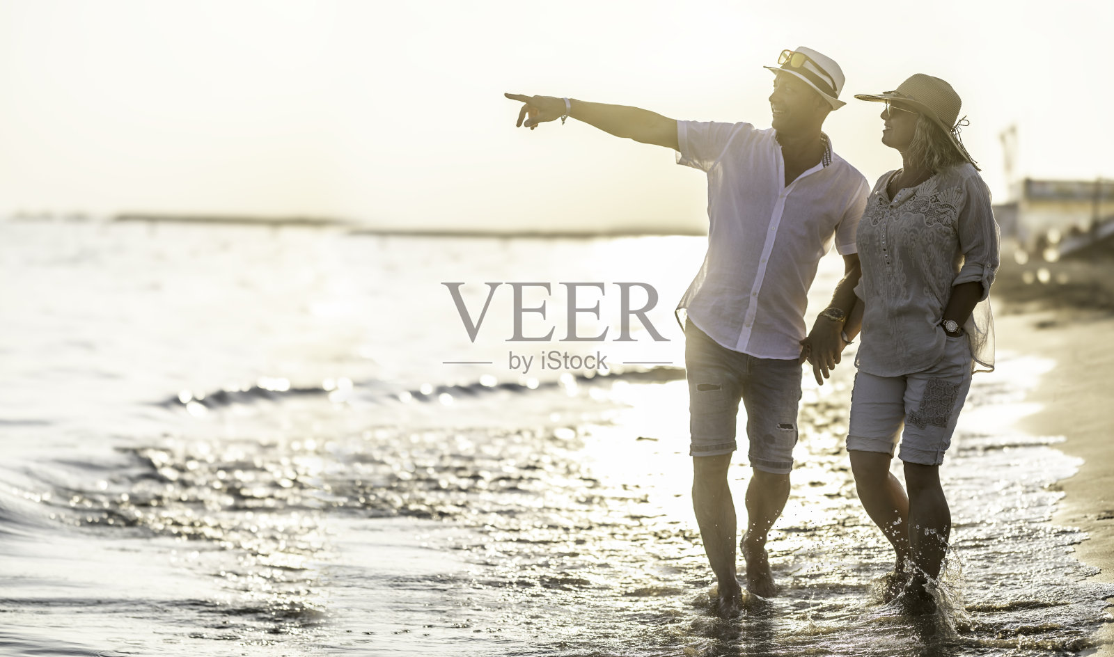 日落时分，一对中年夫妇在海滩上，男人指着远处的一点。照片摄影图片