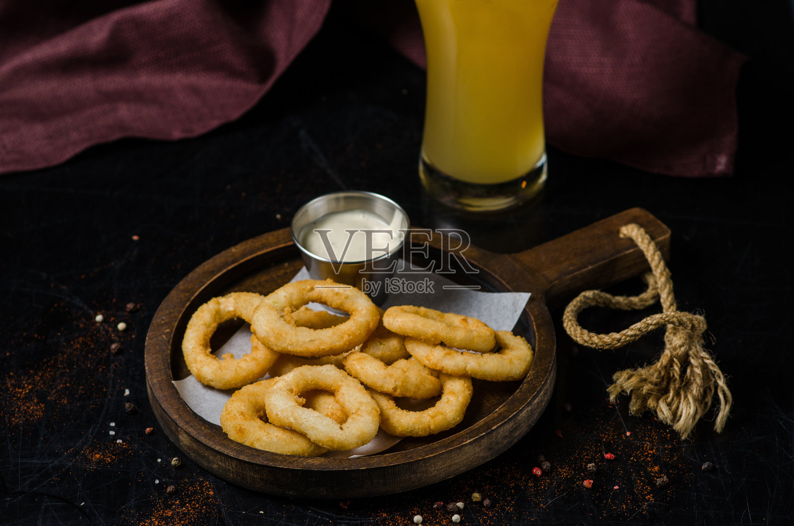 在木板上裹上酱汁的炸洋葱圈。背景里有一大杯啤酒。照片摄影图片
