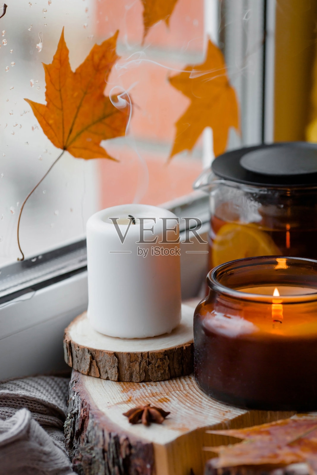 秋天静物与美丽的散景。一杯热茶，一个茶壶，蜂蜜，蜡烛和一条编织的毯子放在窗台上。窗外，秋叶雨点。照片摄影图片