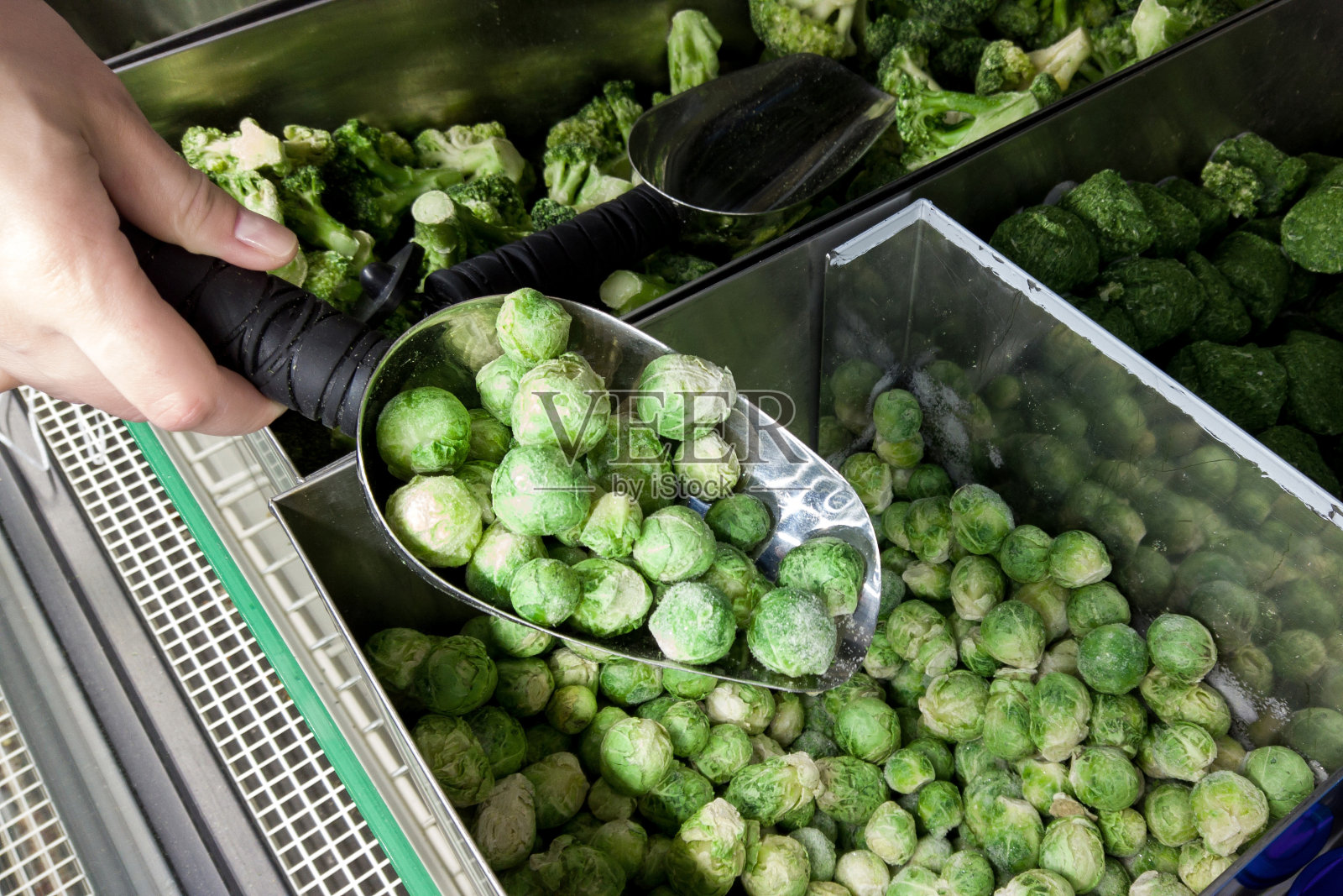 商店冰箱里的冷冻球芽甘蓝。超市里拿着球芽甘蓝勺的女性。照片摄影图片