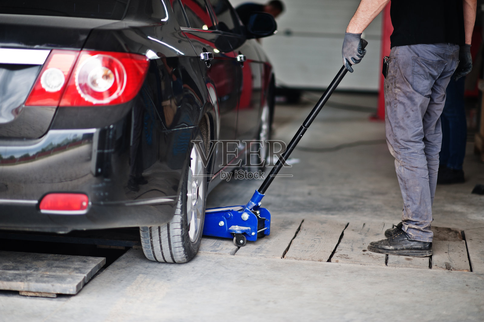 汽车维修保养主题。穿制服的机械师在汽车修理厂工作，用液压千斤顶吊起修理。照片摄影图片