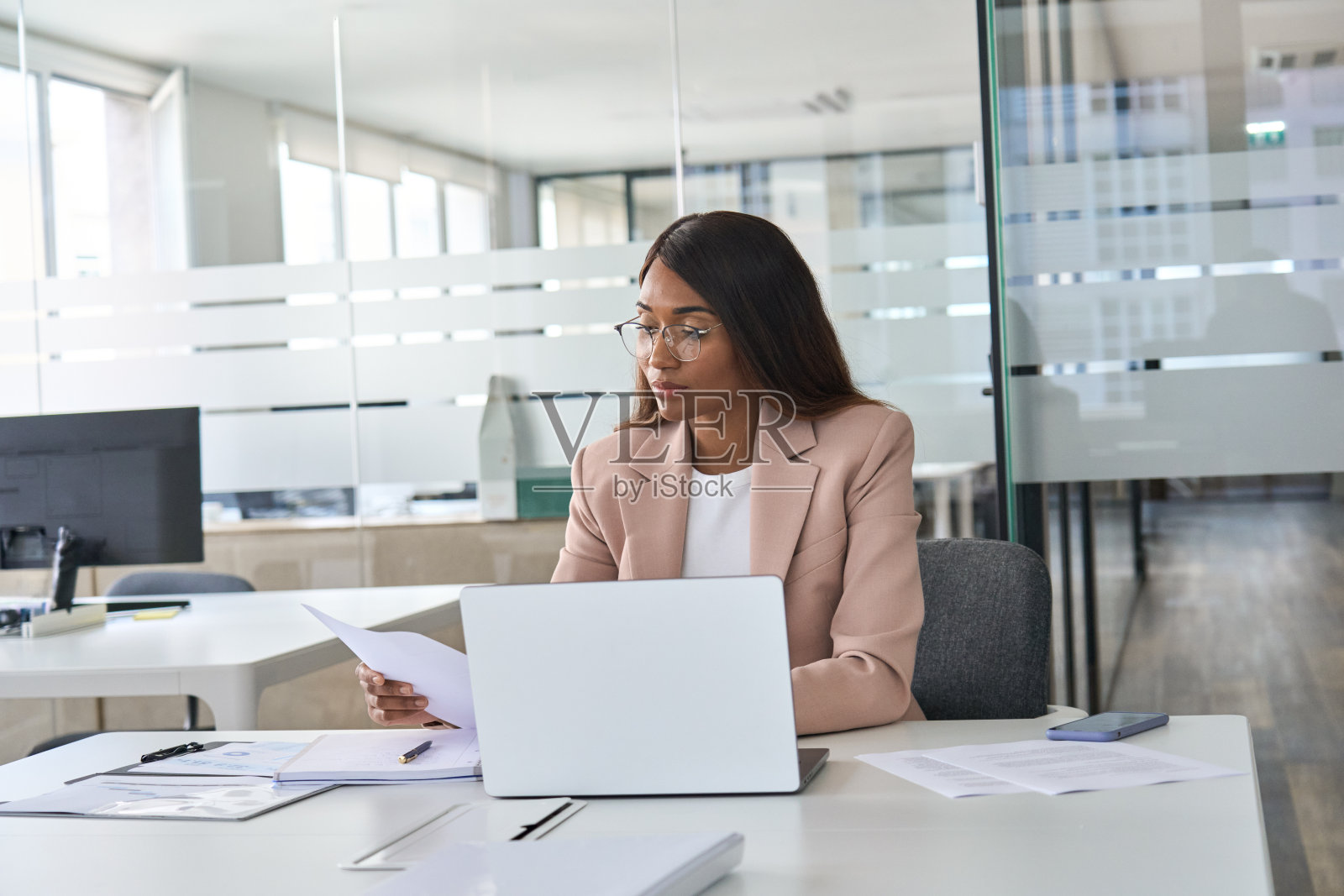 忙碌的年轻女商务主管在办公室用笔记本电脑阅读文件。照片摄影图片