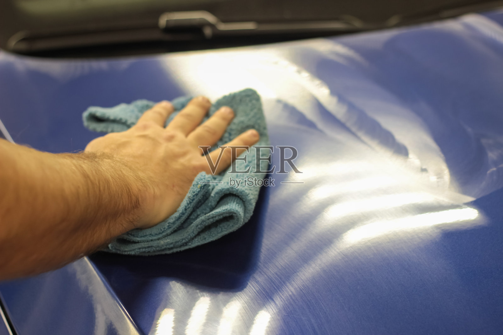 服务人员用超细纤维布擦拭汽车。一名男子手里拿着一根柔软的超细纤维，正在擦拭车身。有选择性的重点。正确洗车和汽车护理的概念。照片摄影图片