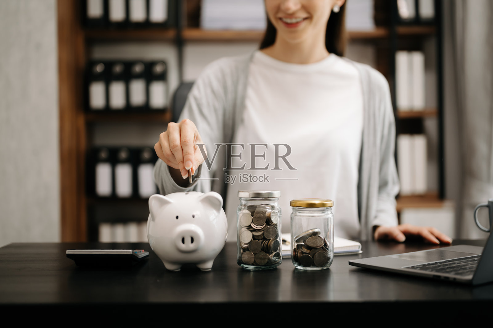 女子拿着硬币放进玻璃杯里，用智能手机和计算器计算概念，为财务会计节省资金。把钱放进存钱罐里照片摄影图片