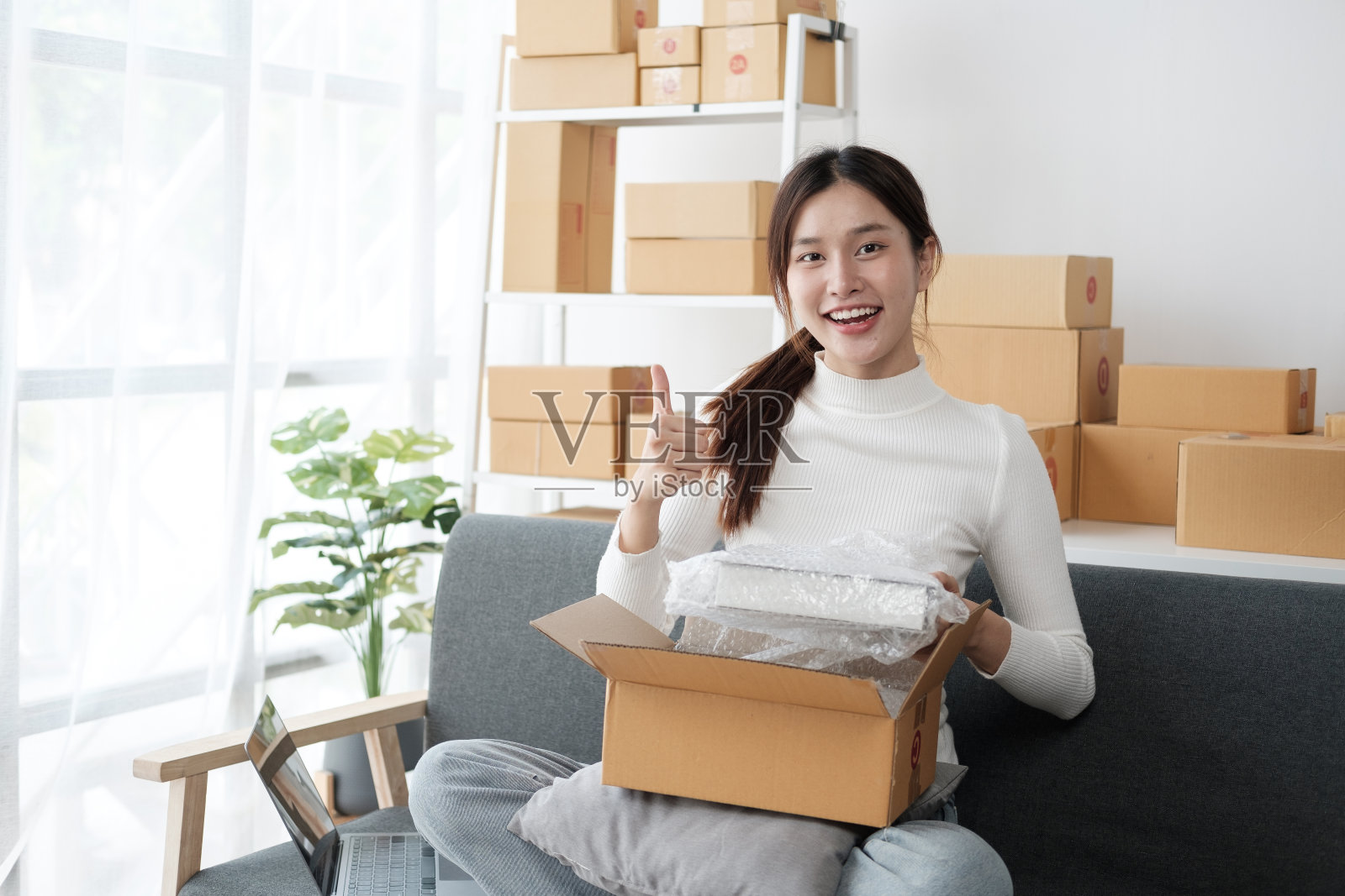 漂亮的亚洲小企业主在她的房间里工作，检查和包装订单给她的客户。照片摄影图片