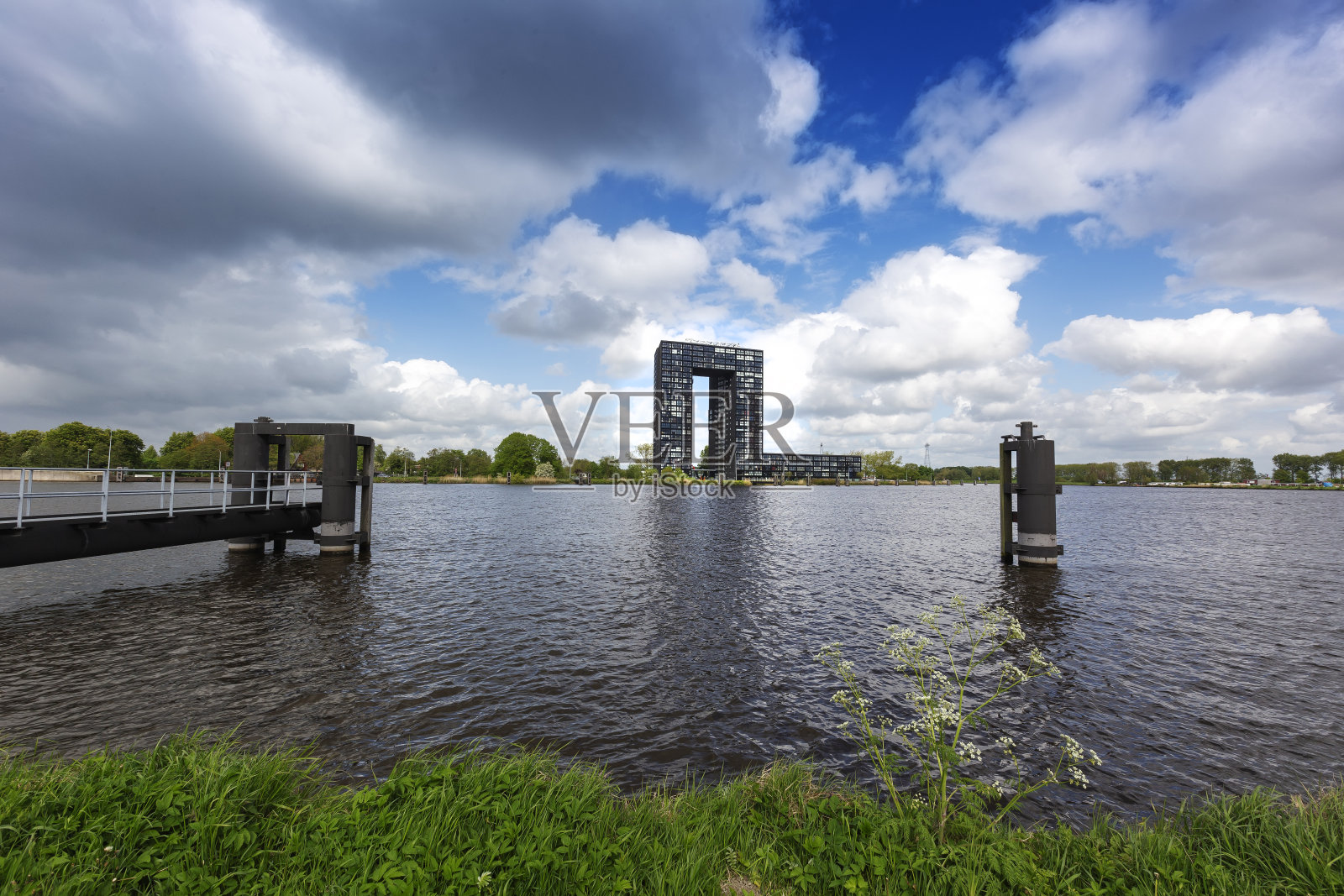 荷兰-格罗宁根水渠，河岸上矗立着一座高大的黑色建筑。前景是一个通往运河的金属码头照片摄影图片