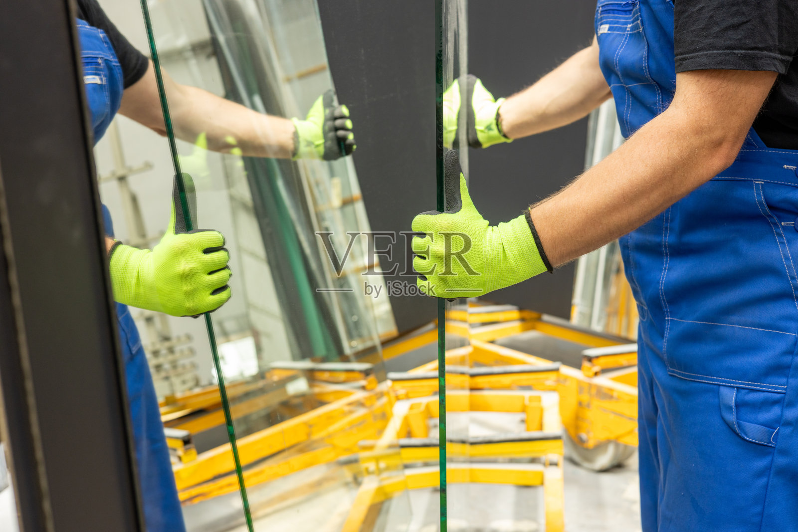 一位玻璃工人从玻璃厂的架子上拿起厚玻璃片，许多镜子引起镜面反射，近距离观察照片摄影图片