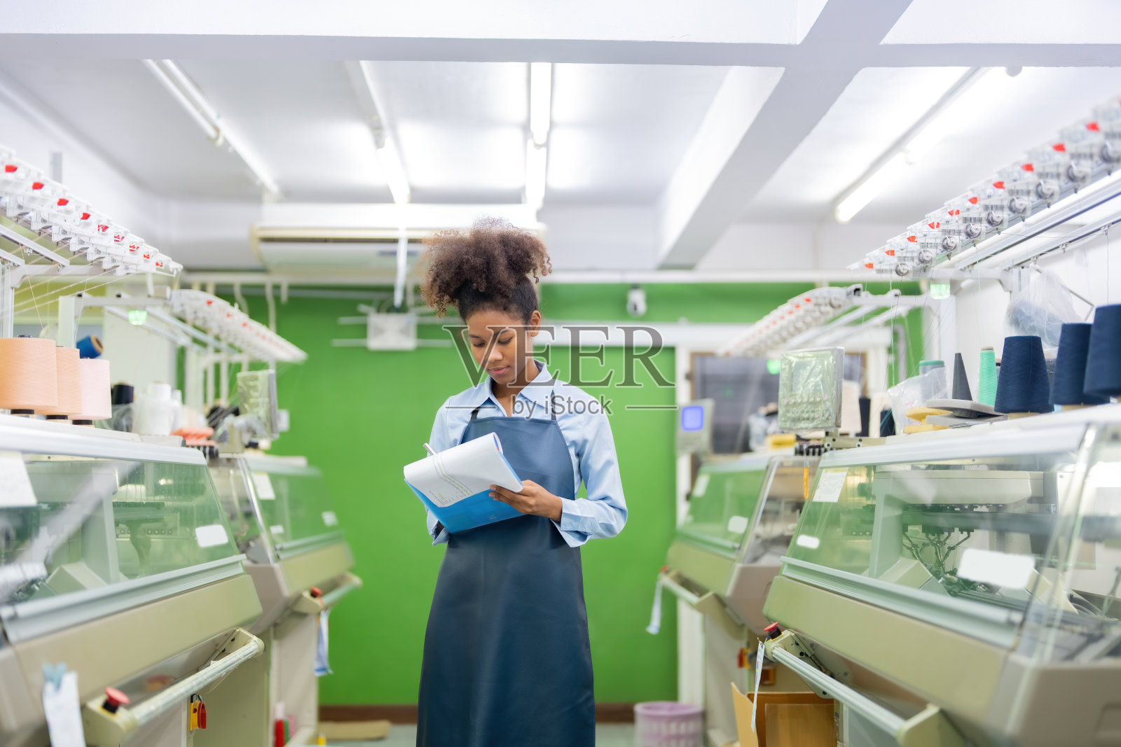 美国女设计师、织布工站在纺织工厂的房间中间，拿着一张单子检查产品订单照片摄影图片