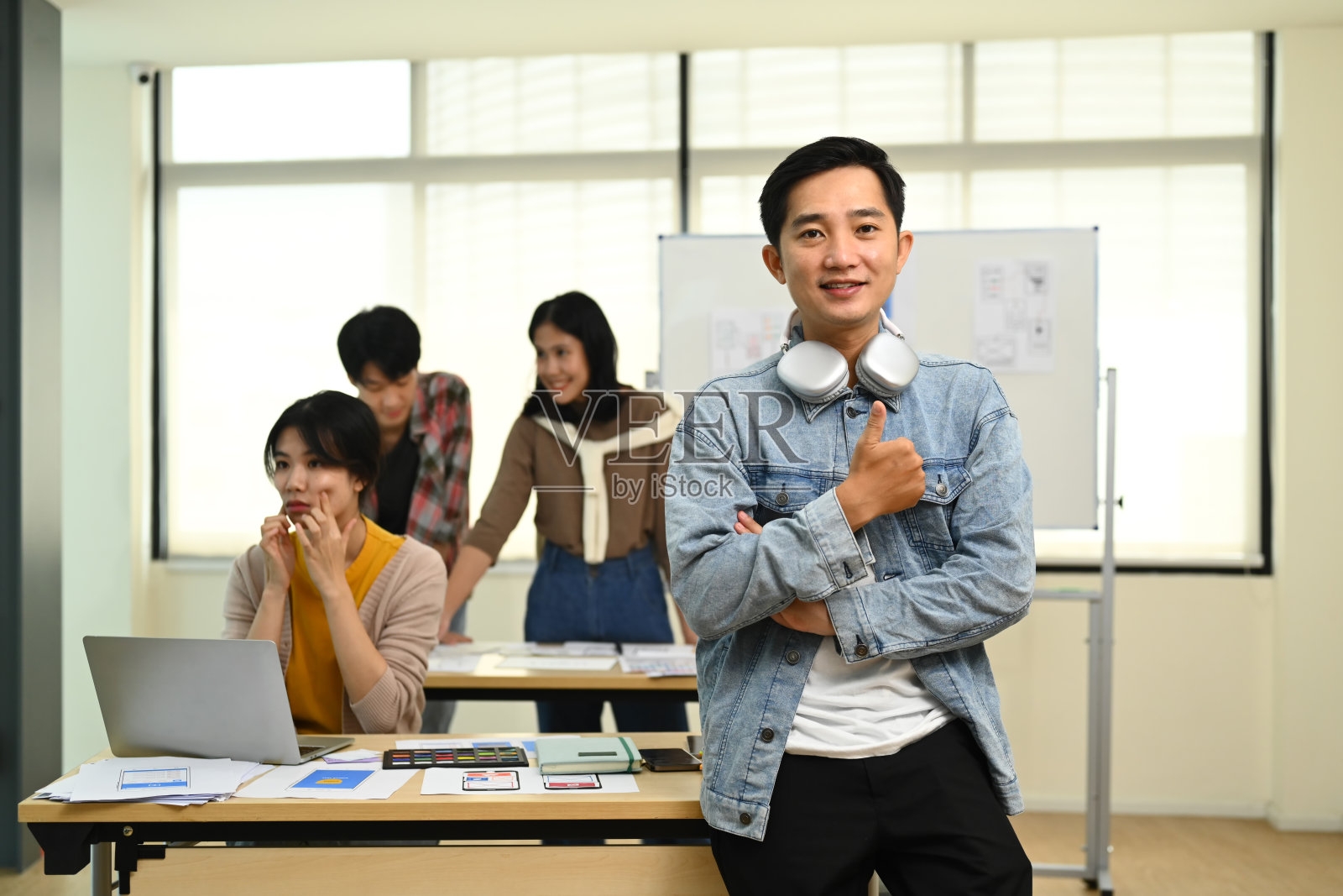 亚洲男性网页开发人员站在创意办公室与他的同事在后台工作的肖像。照片摄影图片