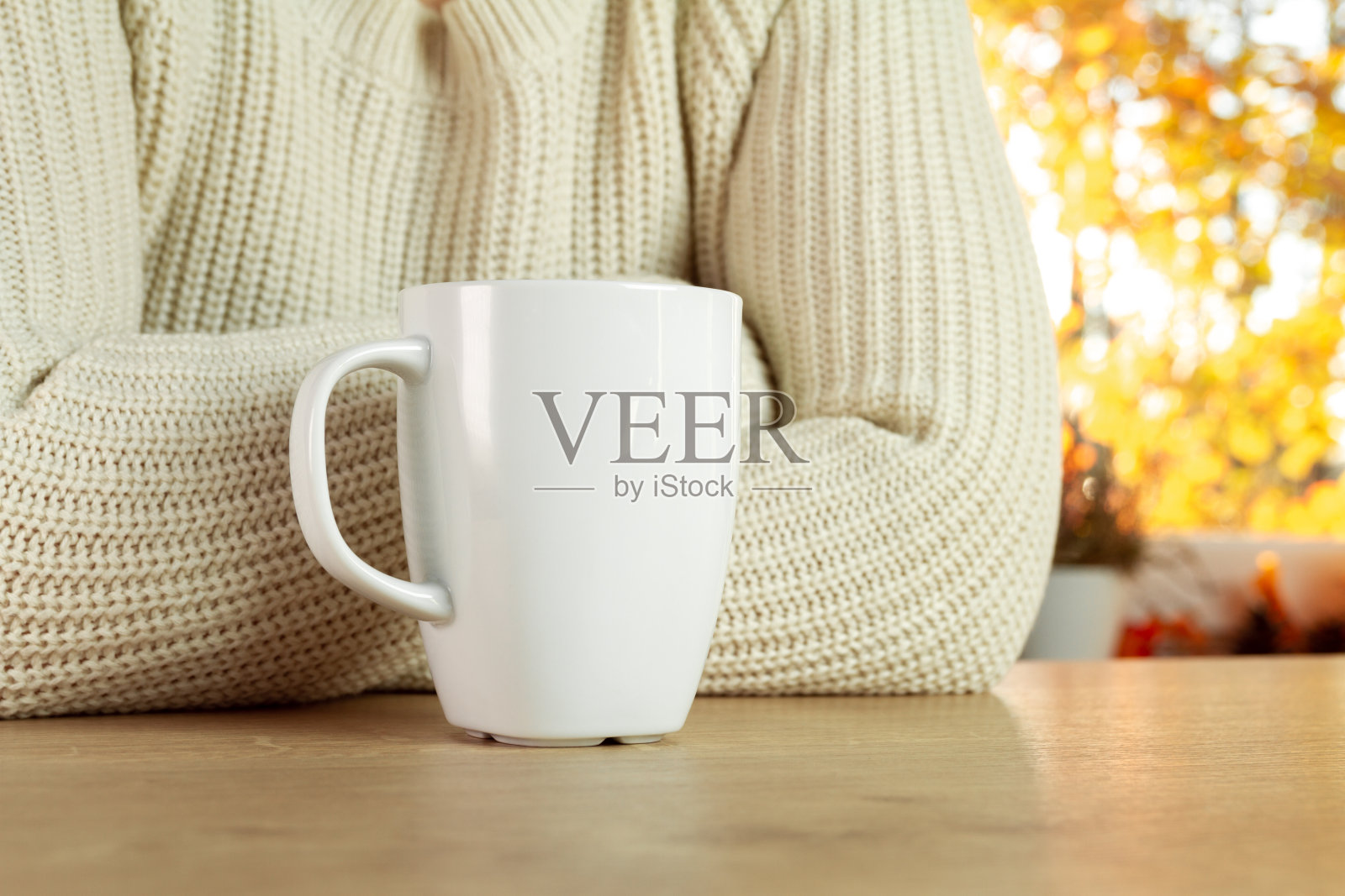 女人靠在桌子上，旁边是一杯热茶或一杯咖啡。背景是秋叶。照片摄影图片