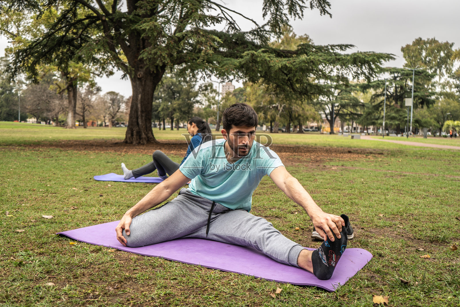 一名中年男子正坐在公园的运动垫上伸展双腿/脚照片摄影图片
