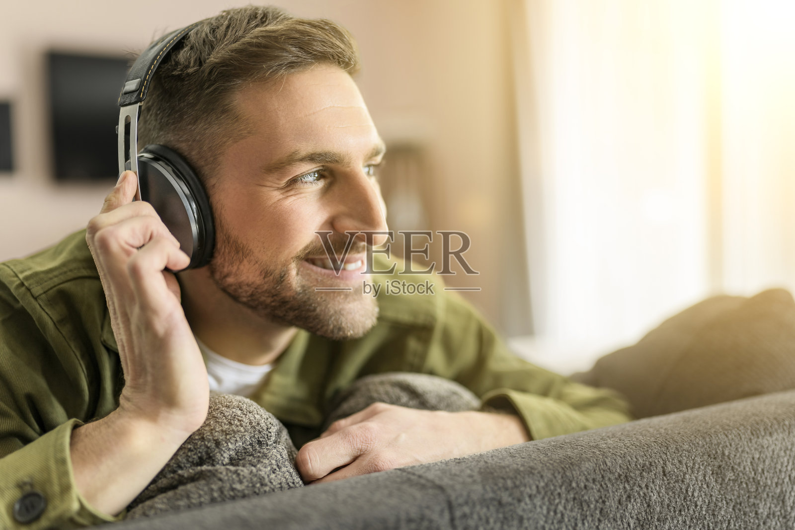 帅哥戴着耳机，坐在舒适的沙发上欣赏音乐。照片摄影图片