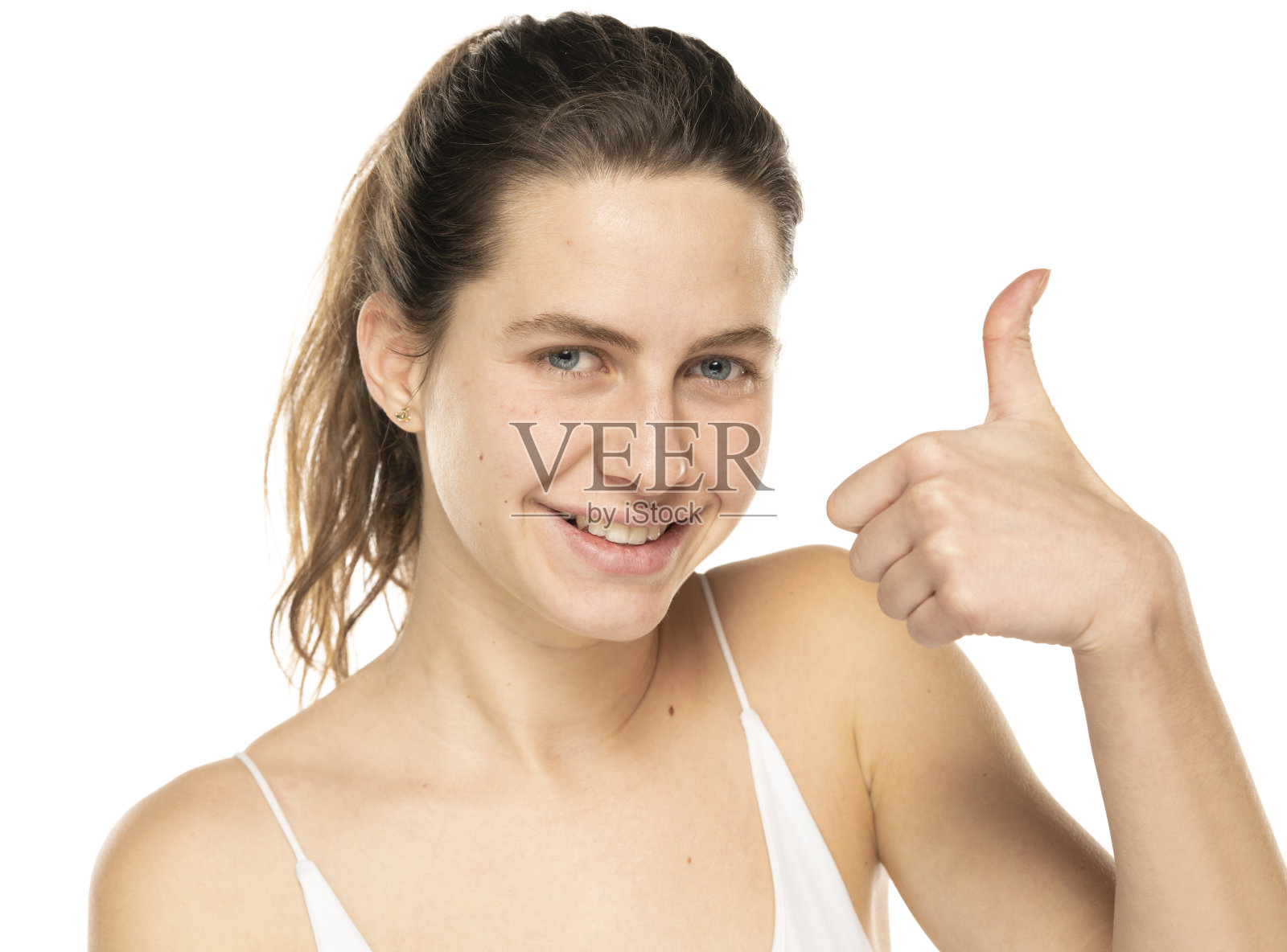 一个年轻女人的肖像，她面带微笑，扎着头发，素颜，在白色的头发上竖起大拇指照片摄影图片