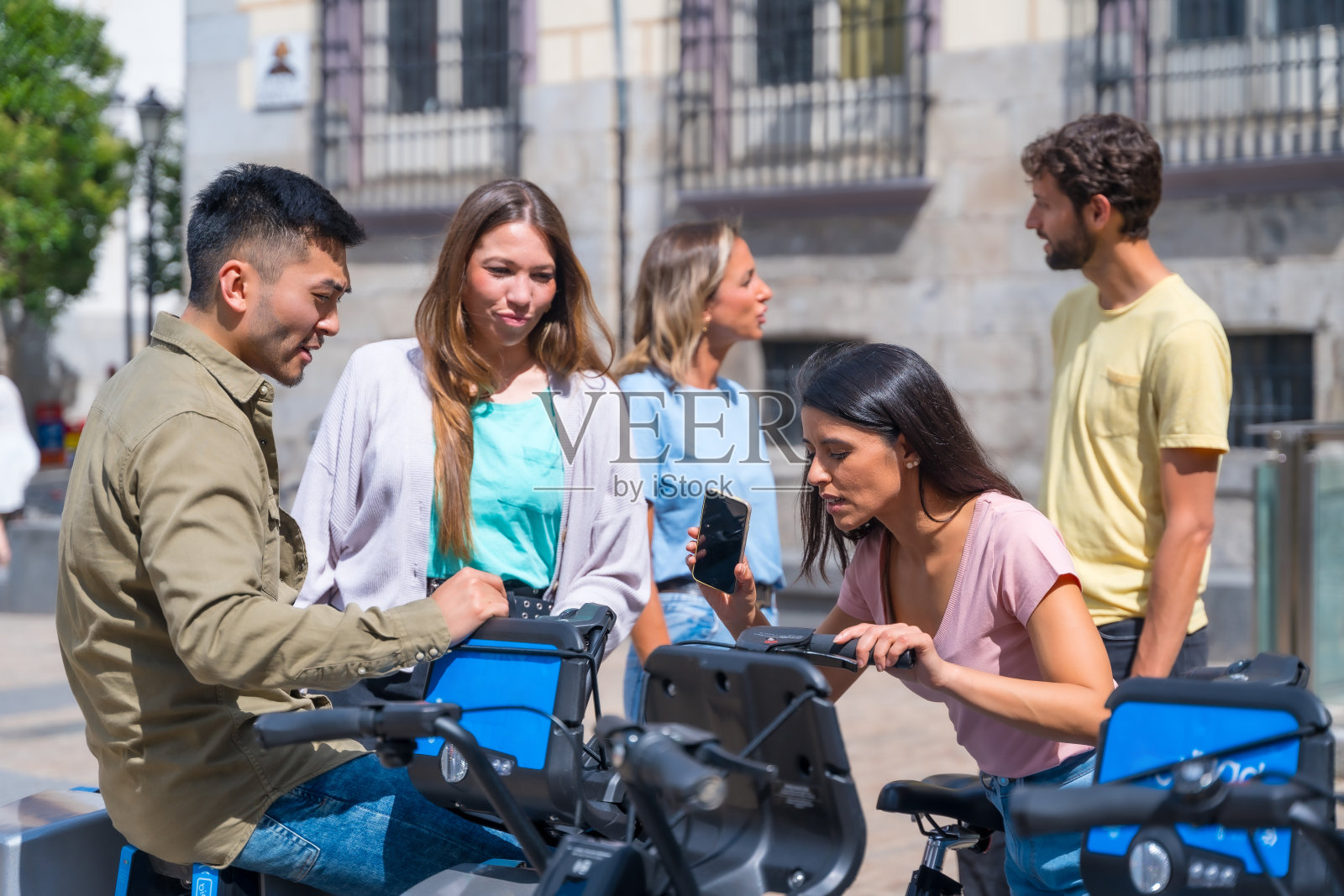 一群多民族的朋友在城市里租自行车玩手机应用程序照片摄影图片