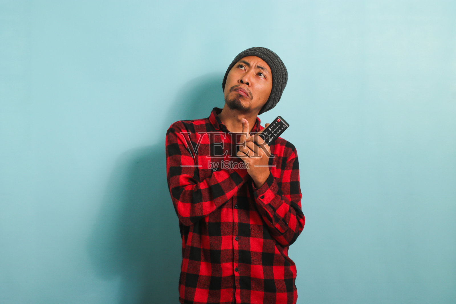 一个忧郁的亚洲年轻人拿着电视遥控器，在蓝色的背景下选择看电影照片摄影图片