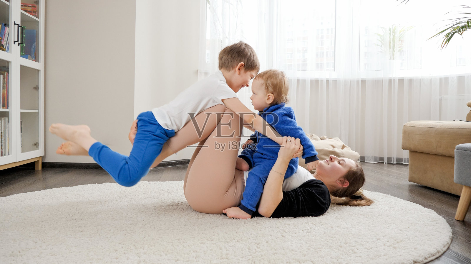 妈妈和两个儿子躺在地板上做健身和伸展运动的有趣照片。家庭保健、积极的生活方式、养育子女和儿童发展照片摄影图片