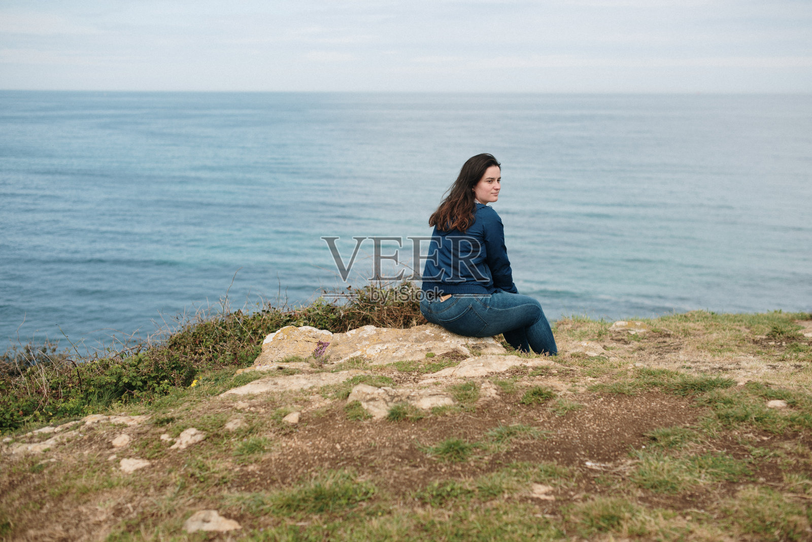 女人坐在海边的岩石上照片摄影图片