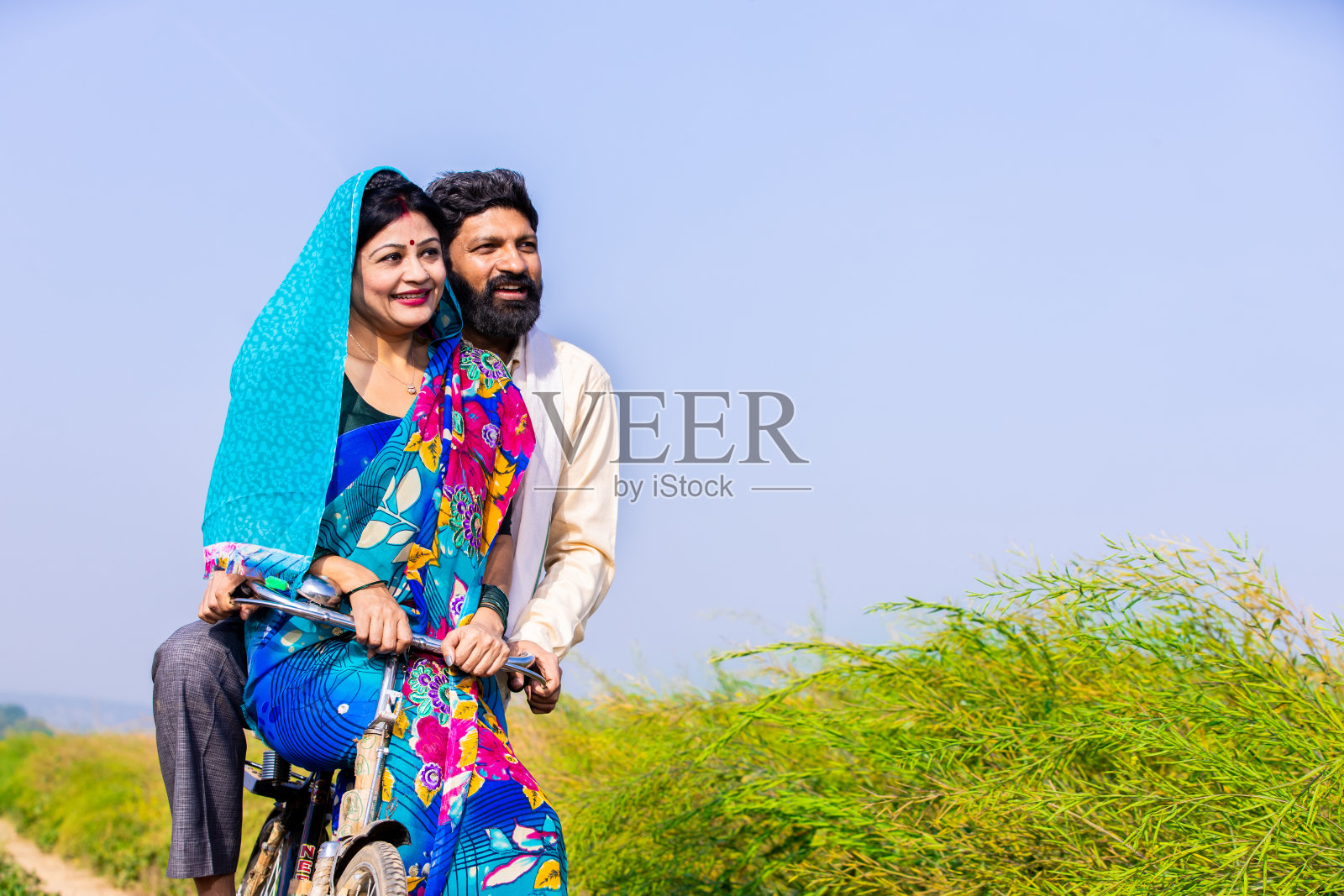 印度农村夫妇在阳光明媚的日子里在农田里骑自行车，复制空间。照片摄影图片