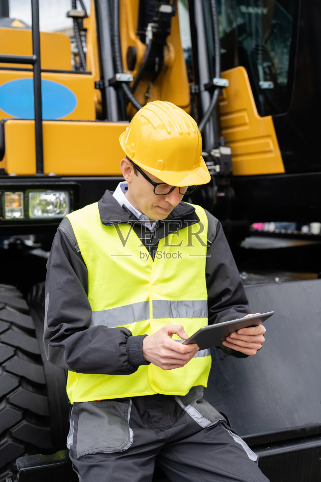 工程师手持平板电脑站在建筑挖掘机旁照片摄影图片