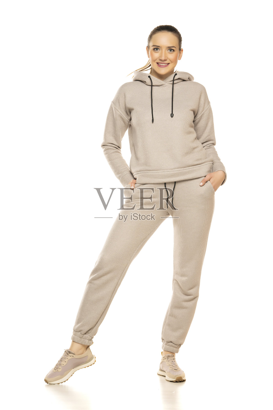 一个身穿灰色运动服、面带微笑的年轻女子在摄影棚白色背景前摆姿势的正面照片照片摄影图片