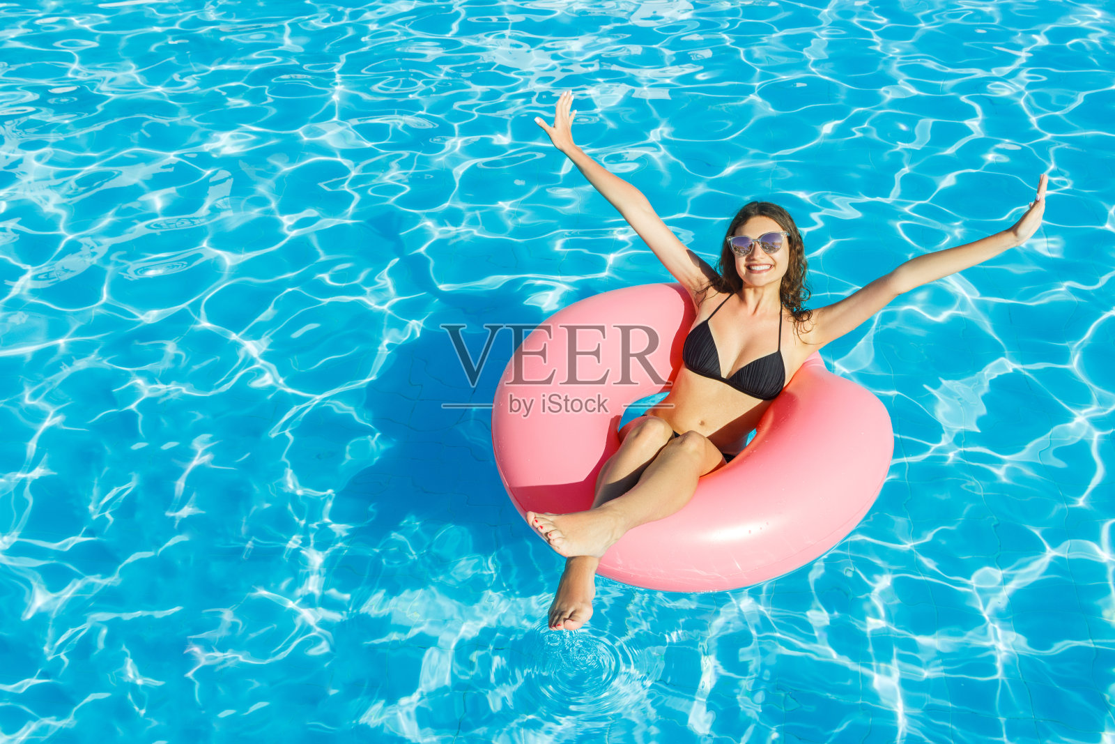 戴墨镜的比基尼美女在粉色泳圈上放松照片摄影图片