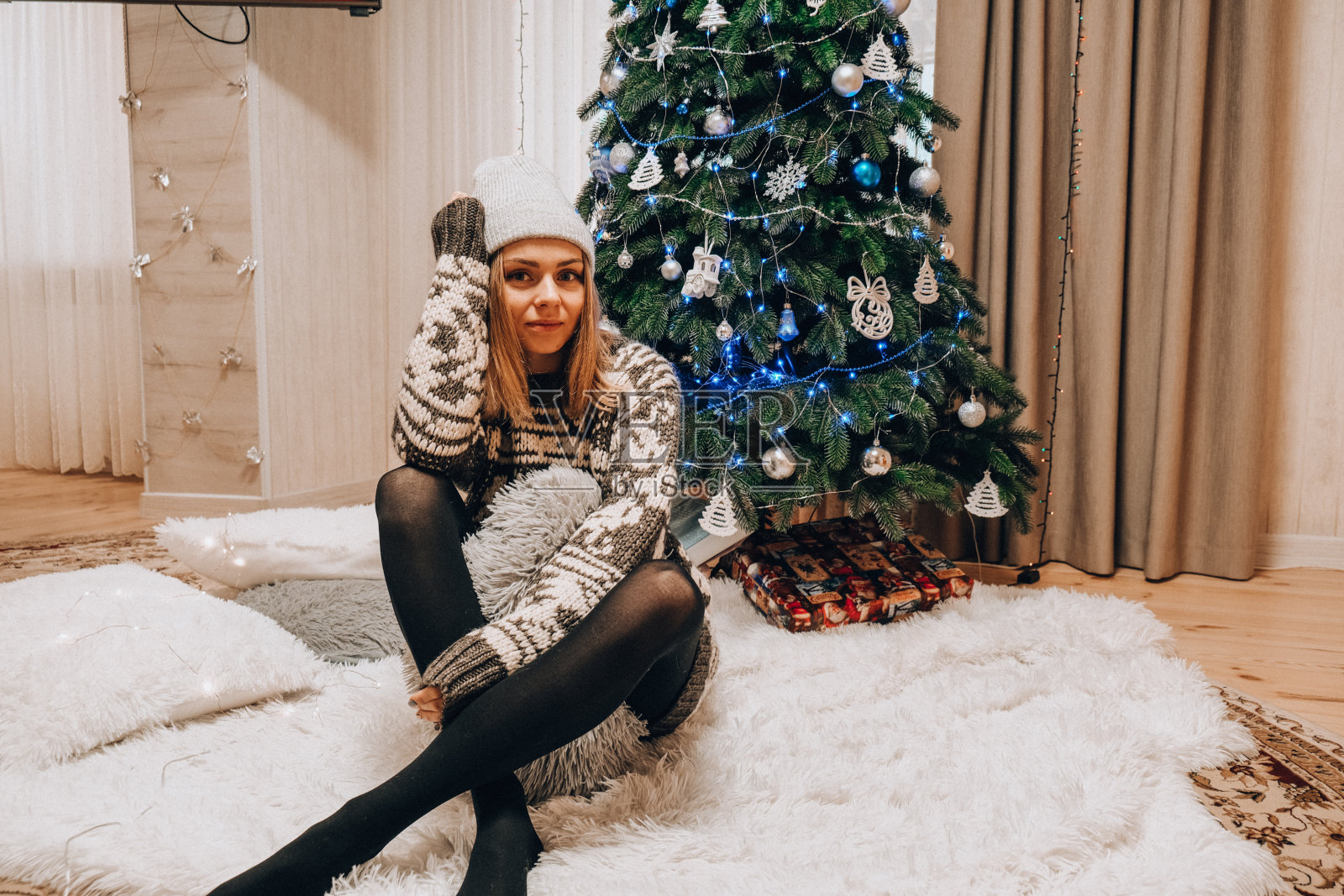 漂亮的年轻女孩坐在圣诞树旁边。新年装饰。家庭内部。寒假照片摄影图片