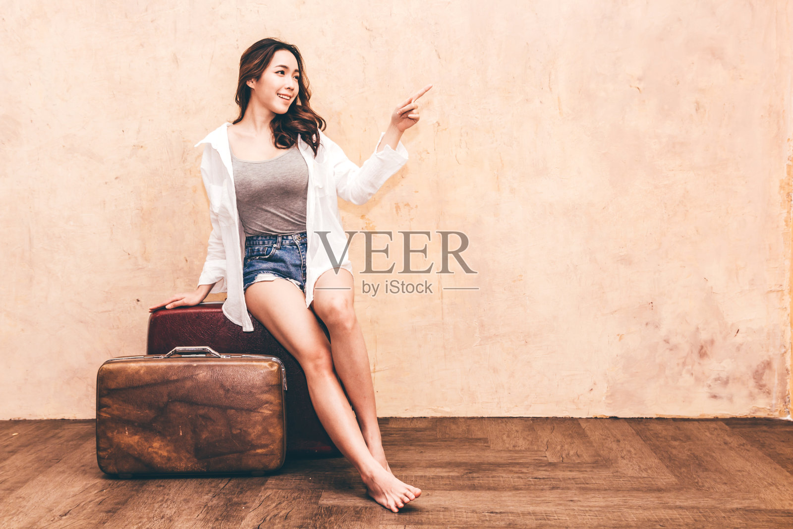 美丽的旅行者女人坐在老式的棕色旅行行李箱与墙的背景照片摄影图片