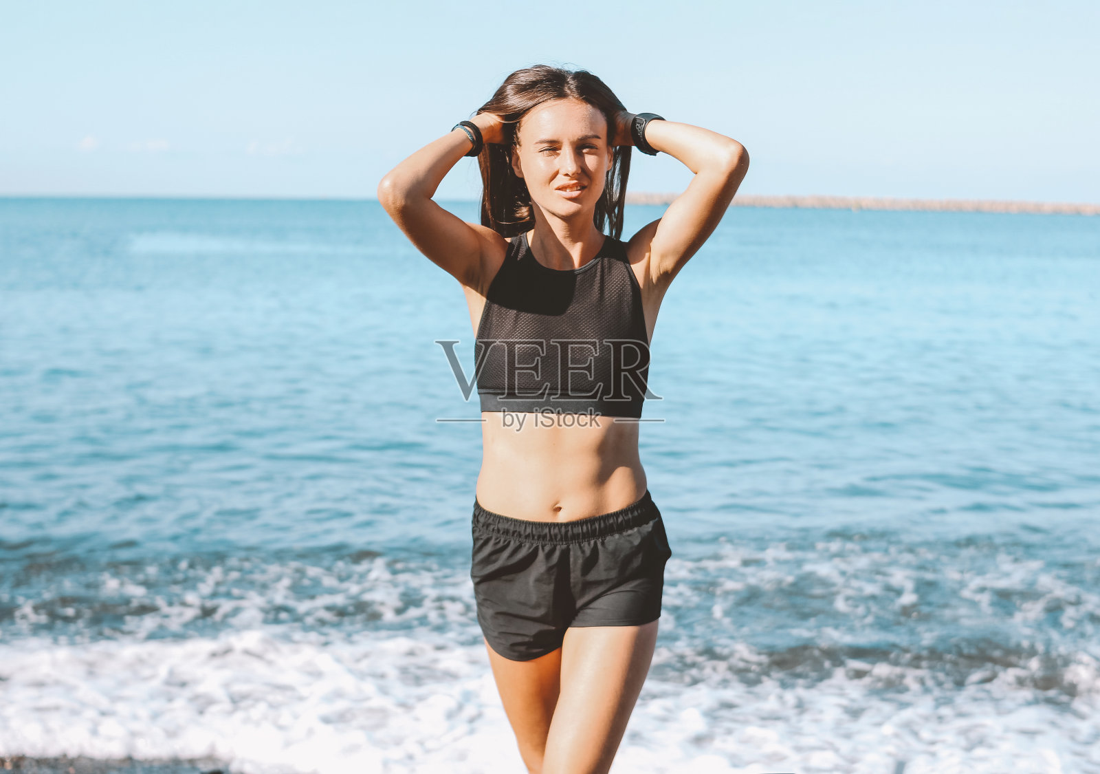 年轻苗条的运动长发性感的女人穿着运动服在海边，健康的生活方式照片摄影图片