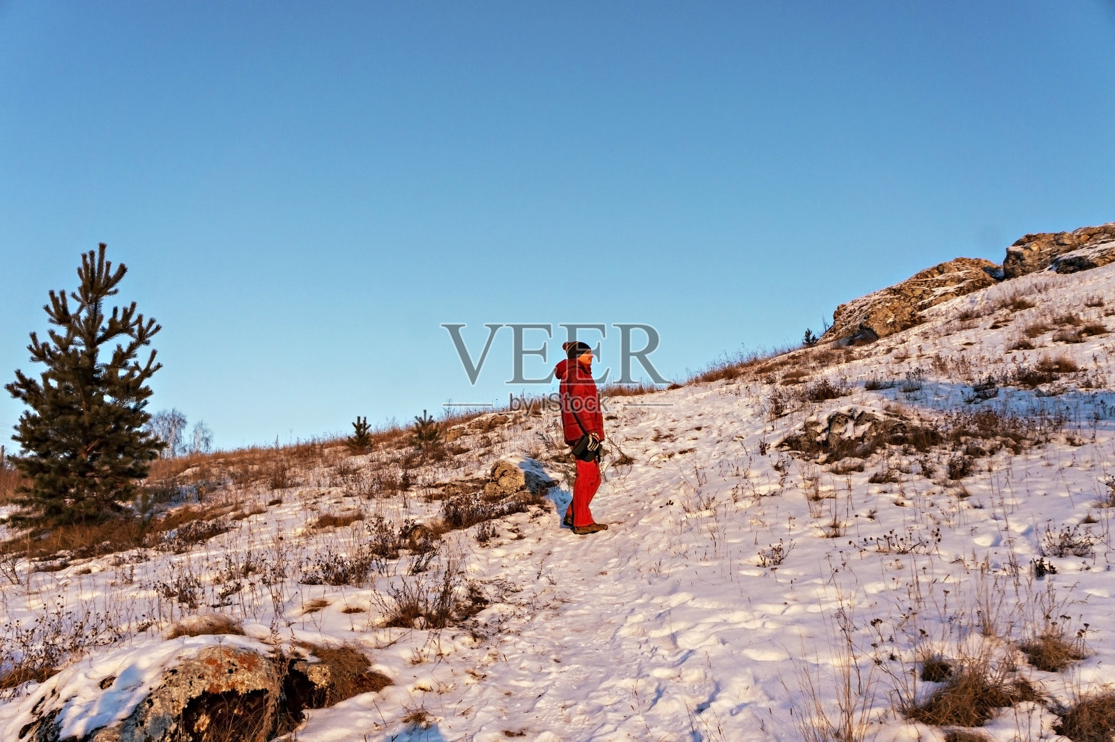 冬天，身穿红色冬装的年轻人顶着蓝天徒步登山。照片摄影图片